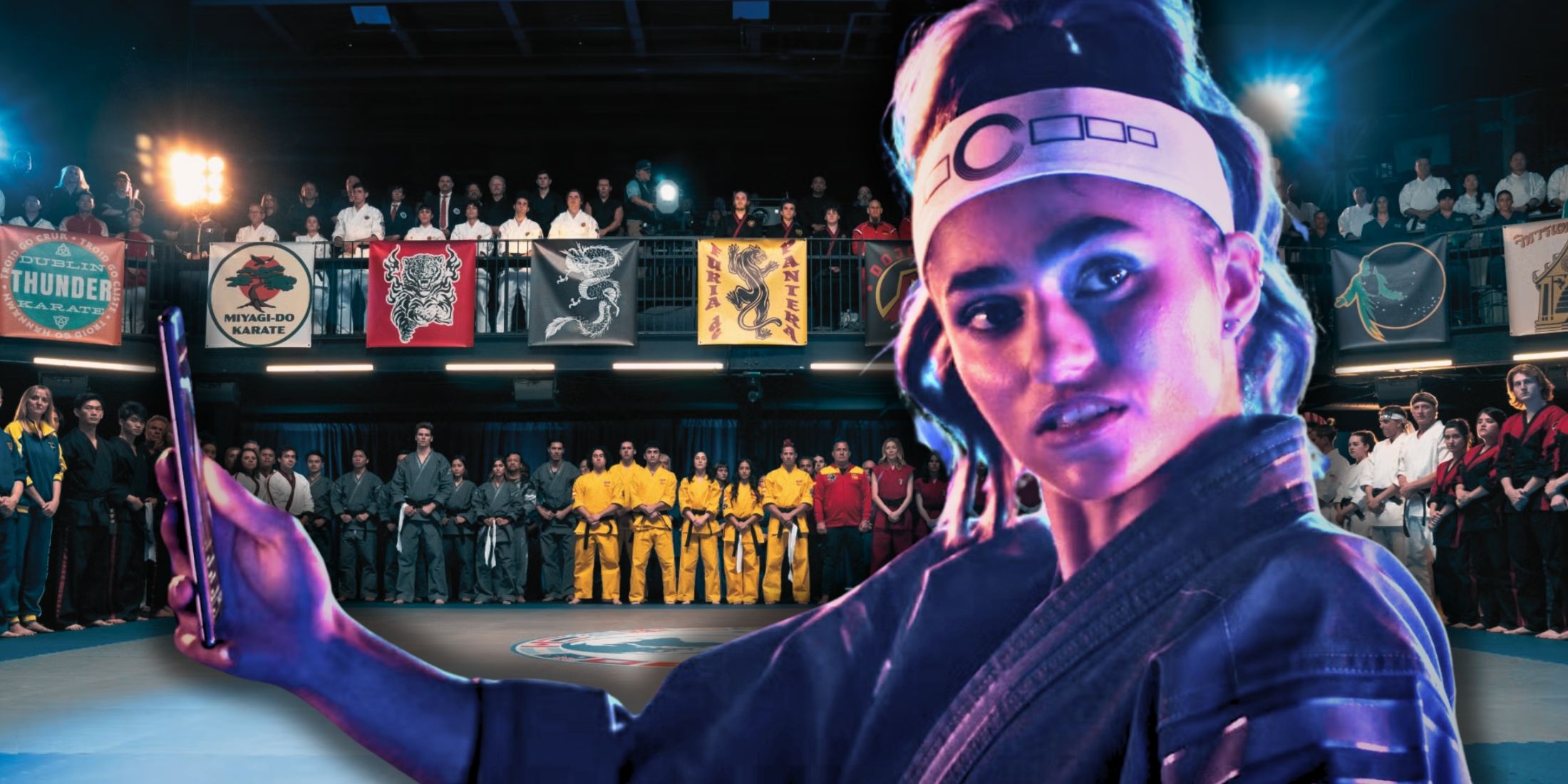 Zara with her phone out in front of her over an image of the Sekai Taikai teams in Cobra Kai