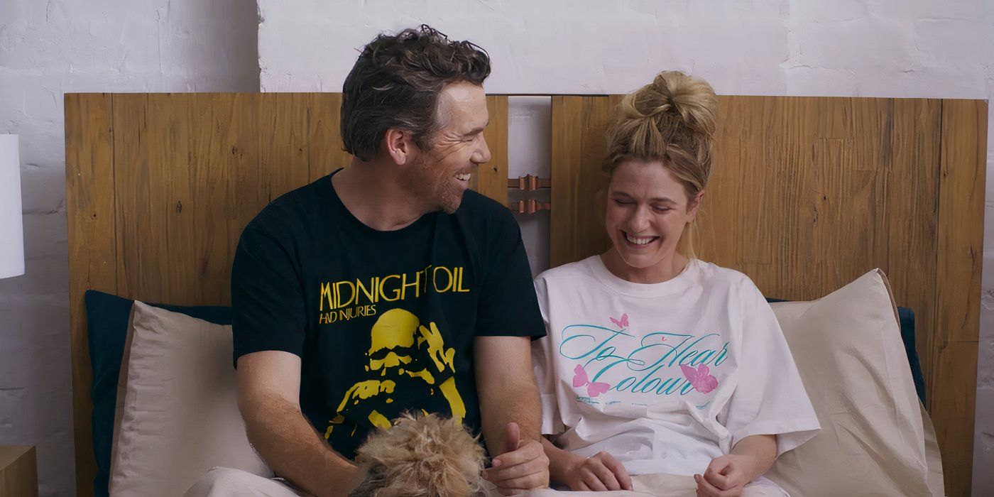 Gordon and Ashley laugh together while sitting in bed in Colin from Accounts