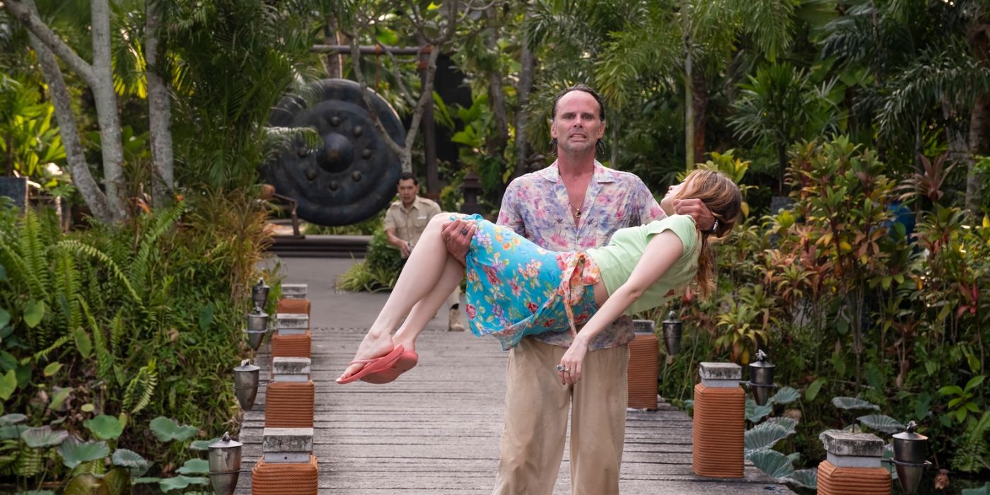 Gaitok (Tayme Thapthimthong) pointing a gun as Rick (Walton Goggins) carries a dying Chelsea (Aimee Lou Wood) in The White Lotus season 3, episode 8.