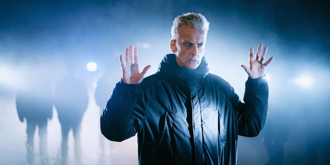 Gideon (Peter Capaldi) with his hands raised while people shine lights at him in The Devil&rsquo;s Hour.
