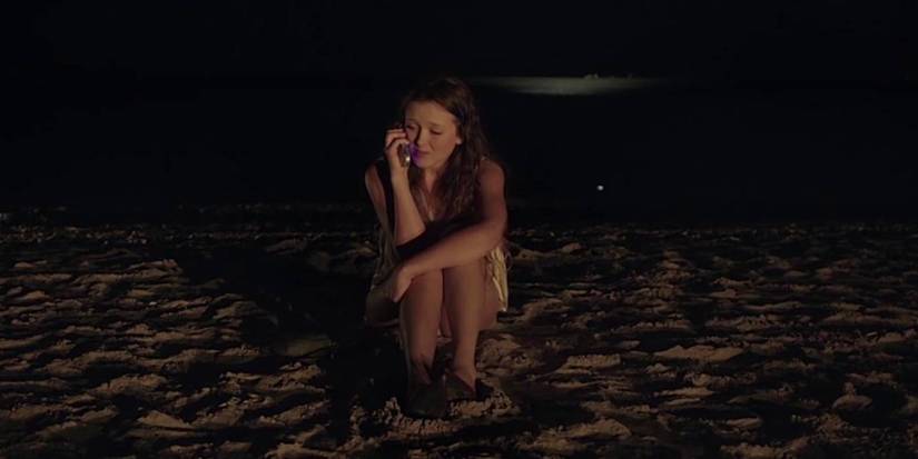 Bailey Spry as Annie Marshall sitting on the beach in It Follows.