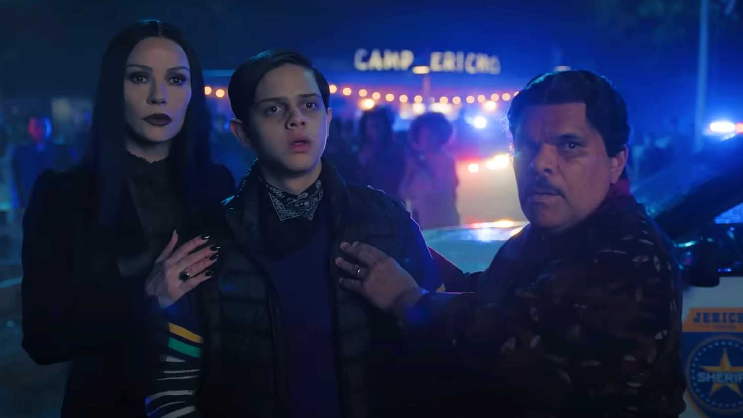 Morticia and Gomez Addams nervously holding onto Pugsley near a police car in Wednesday season 2