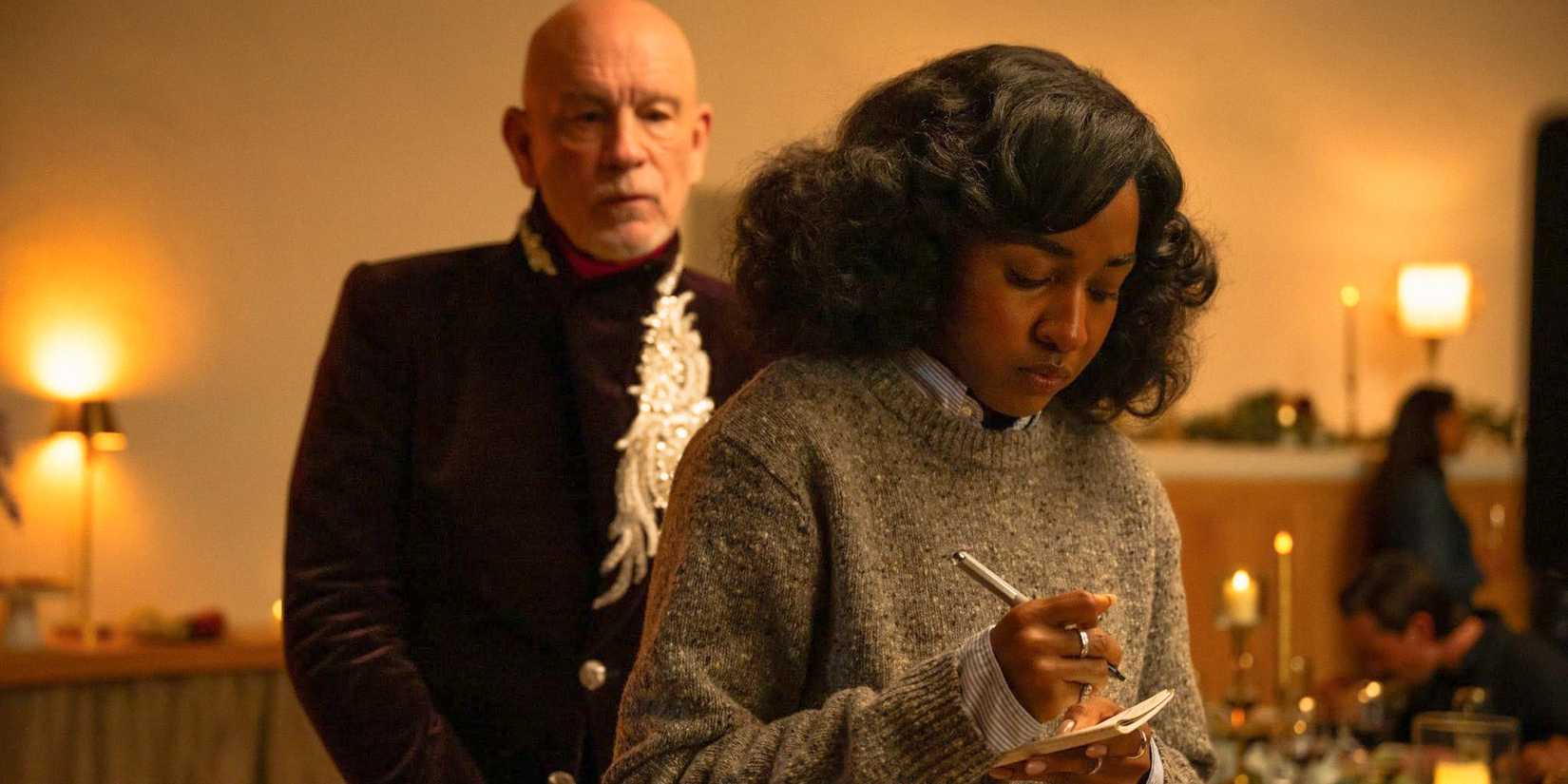 Ariel Ecton (Ayo Edebiri) taking notes while Alfred Moretti (John Malkovich) watches her intrigued in Opus (2025)