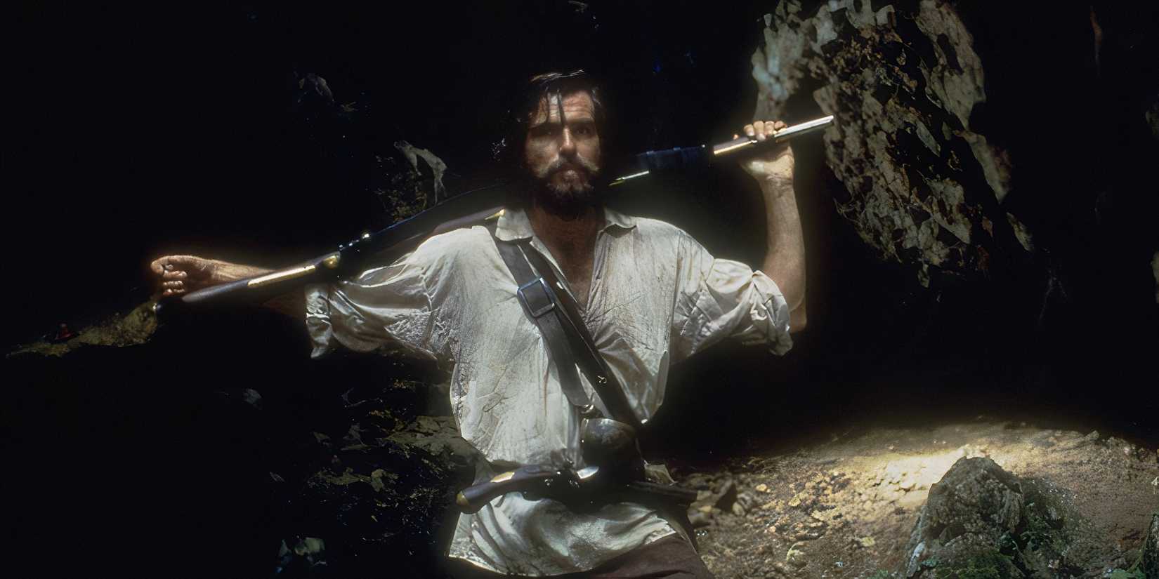 Pierce Brosnan standing with a rifle over his shoulders in Robinson Crusoe
