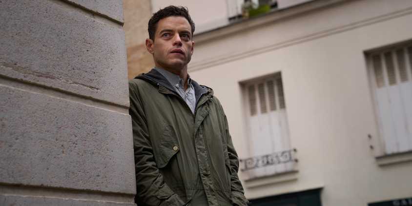 Rami Malek standing behind a wall in The Amateur