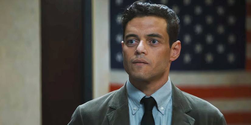 Rami Malek Standing in Front of a Flag in The Amateur
