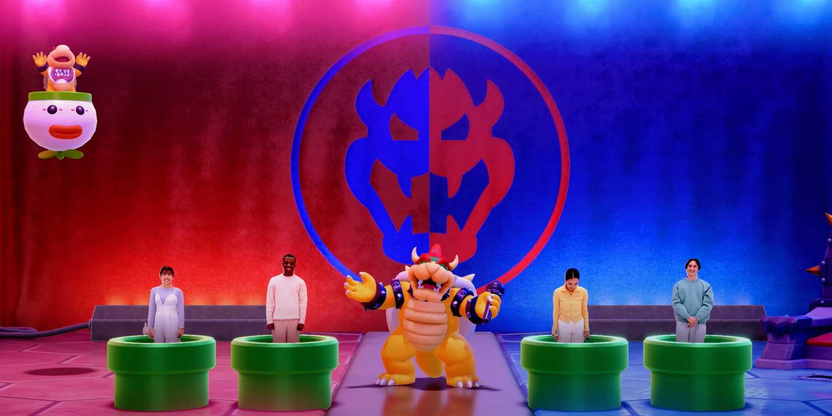 Four players emerge in pipes as Bowser laughs in the center with a microphone in his hand in the Switch 2 Edition of Super Mario Party Jamboree. Bowser Jr. also laughs while flying above the stage.