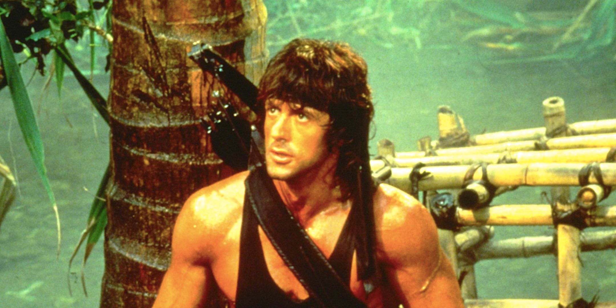 Sylvester Stallone's Rambo stands in the jungle beside a bamboo cage from First Blood Part II