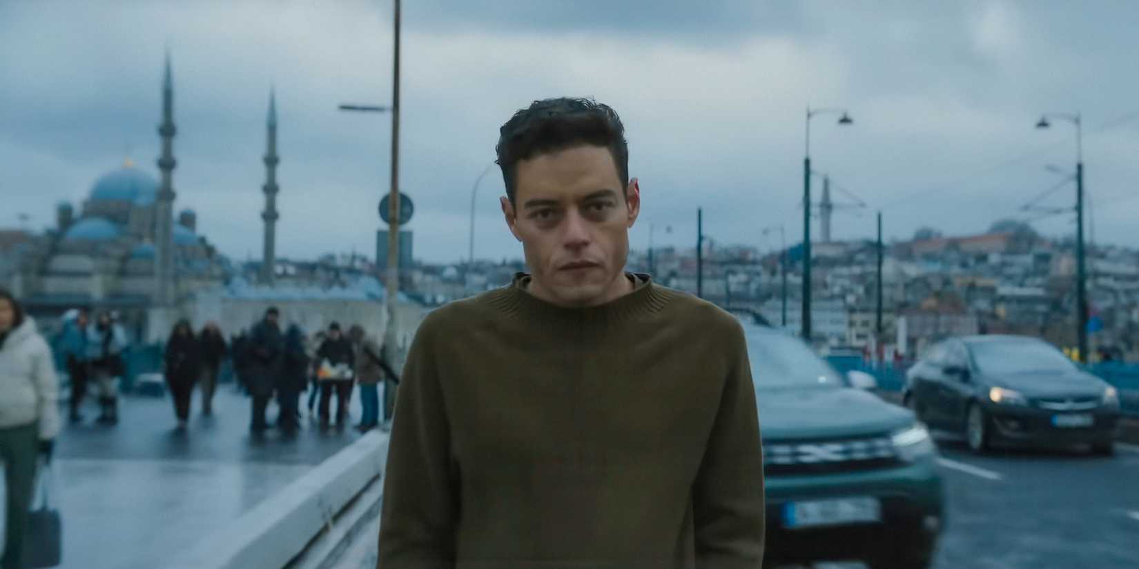 Rami Malek as Heller walking down the street with an intense look in The Amateur