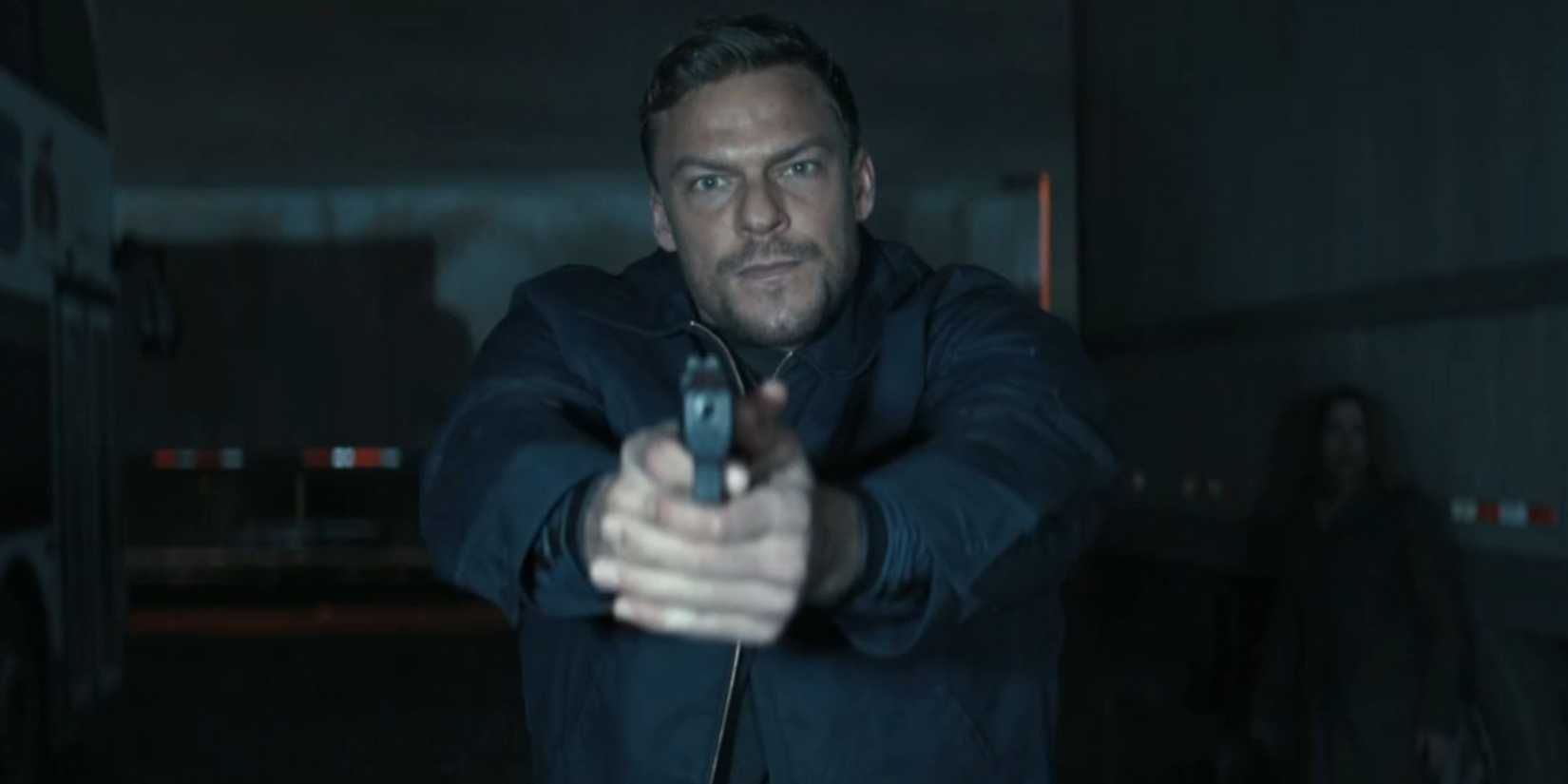 Alan Ritchson aiming his gun at the screen as Reacher