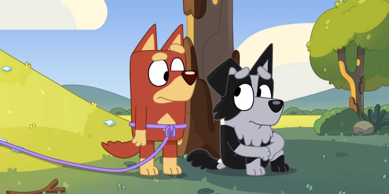 Rusty with a rope tied around his waist standing next to Mackenzie, who is sitting under a tree