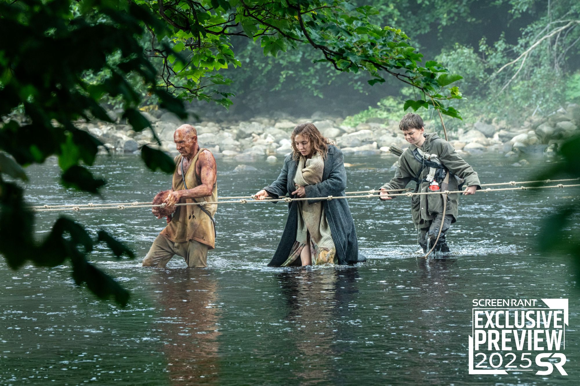 Ralph Fiennes, Jodie Comer, and Alfie Williams holding onto a rope while walking across a river in 28 Years Later