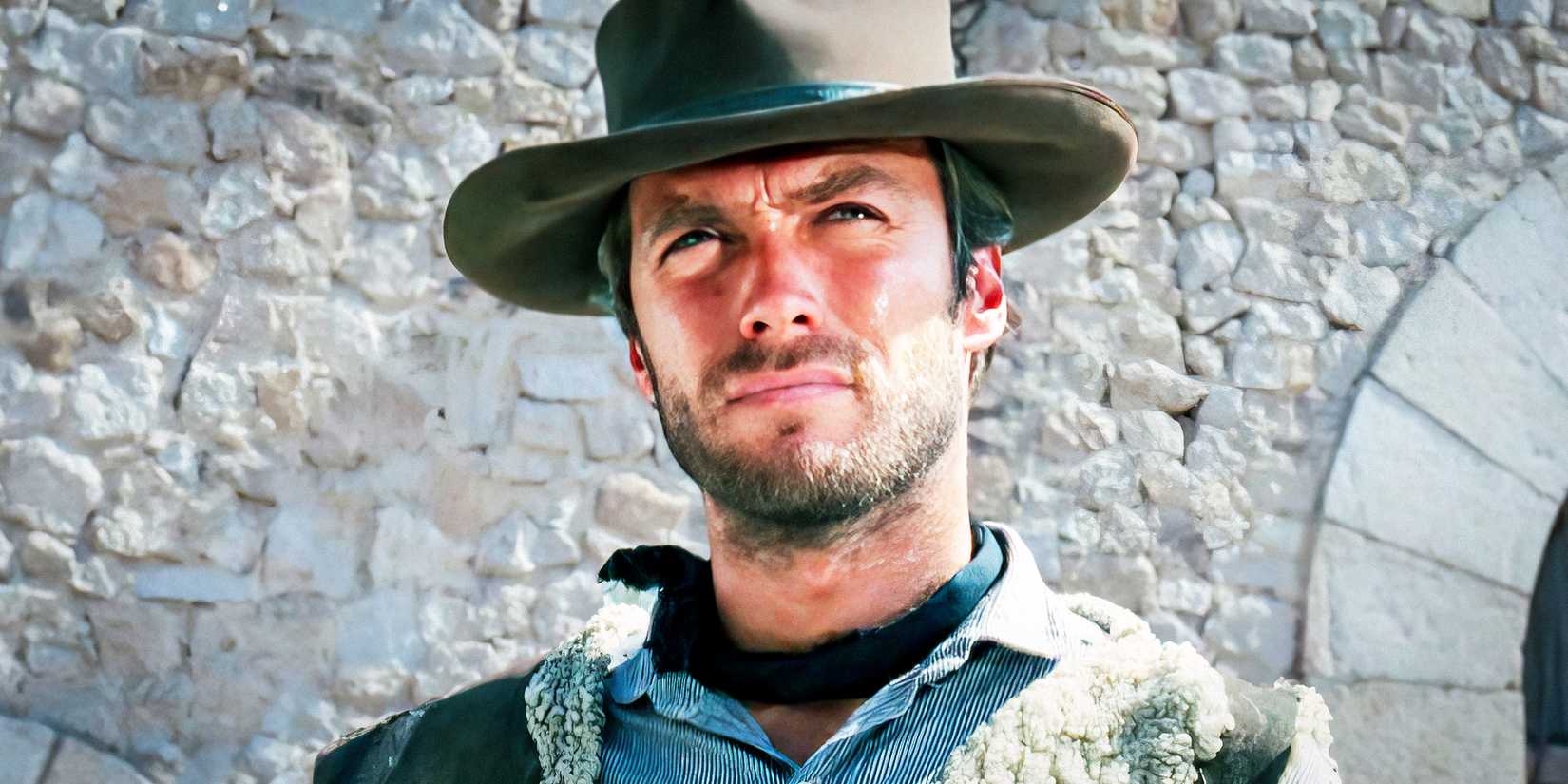 Clint Eastwood as Joe standing in front of a brick wall in A Fistful of Dollars