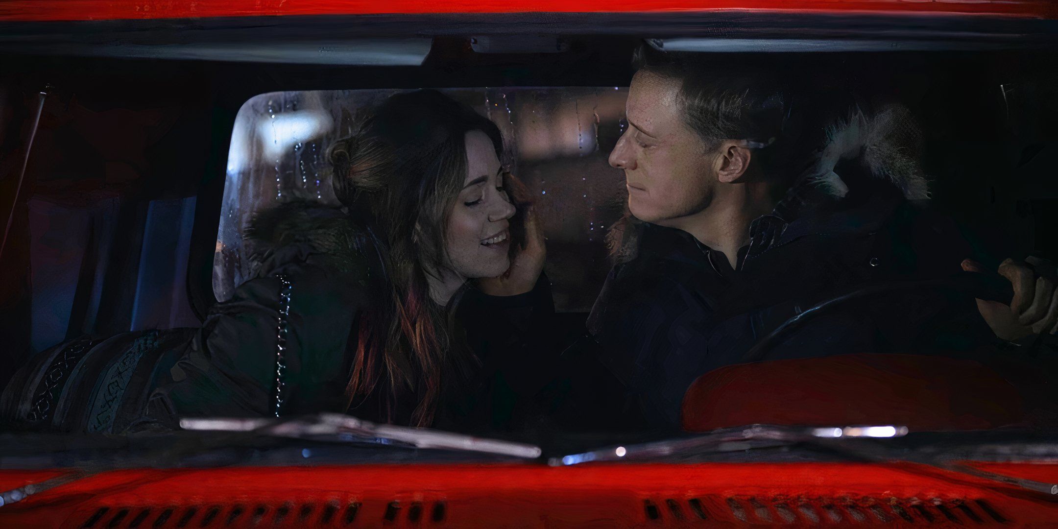 Harry with his hand on D'Arcy's cheek, sitting inside a red truck 
