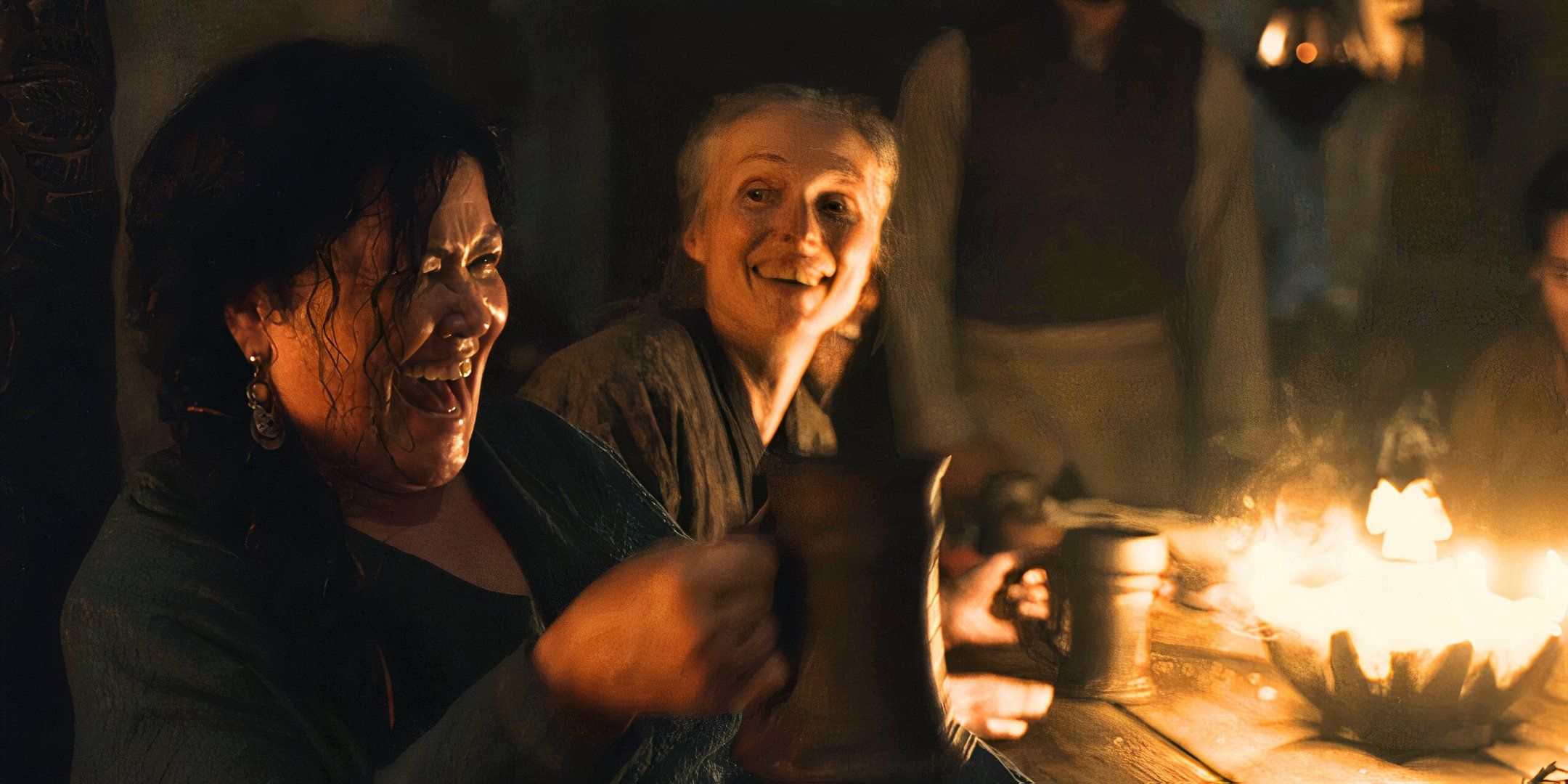 Daise Congar laughing with a mug in front of a fire as a woman smiles behind her