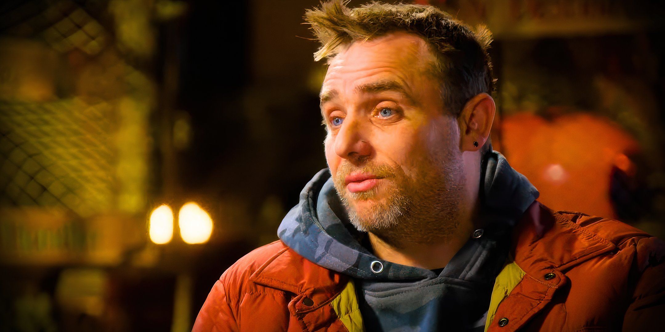 deadliest catch star Jake Anderson looking serious in an orange jacket with a dimly lit interior background
