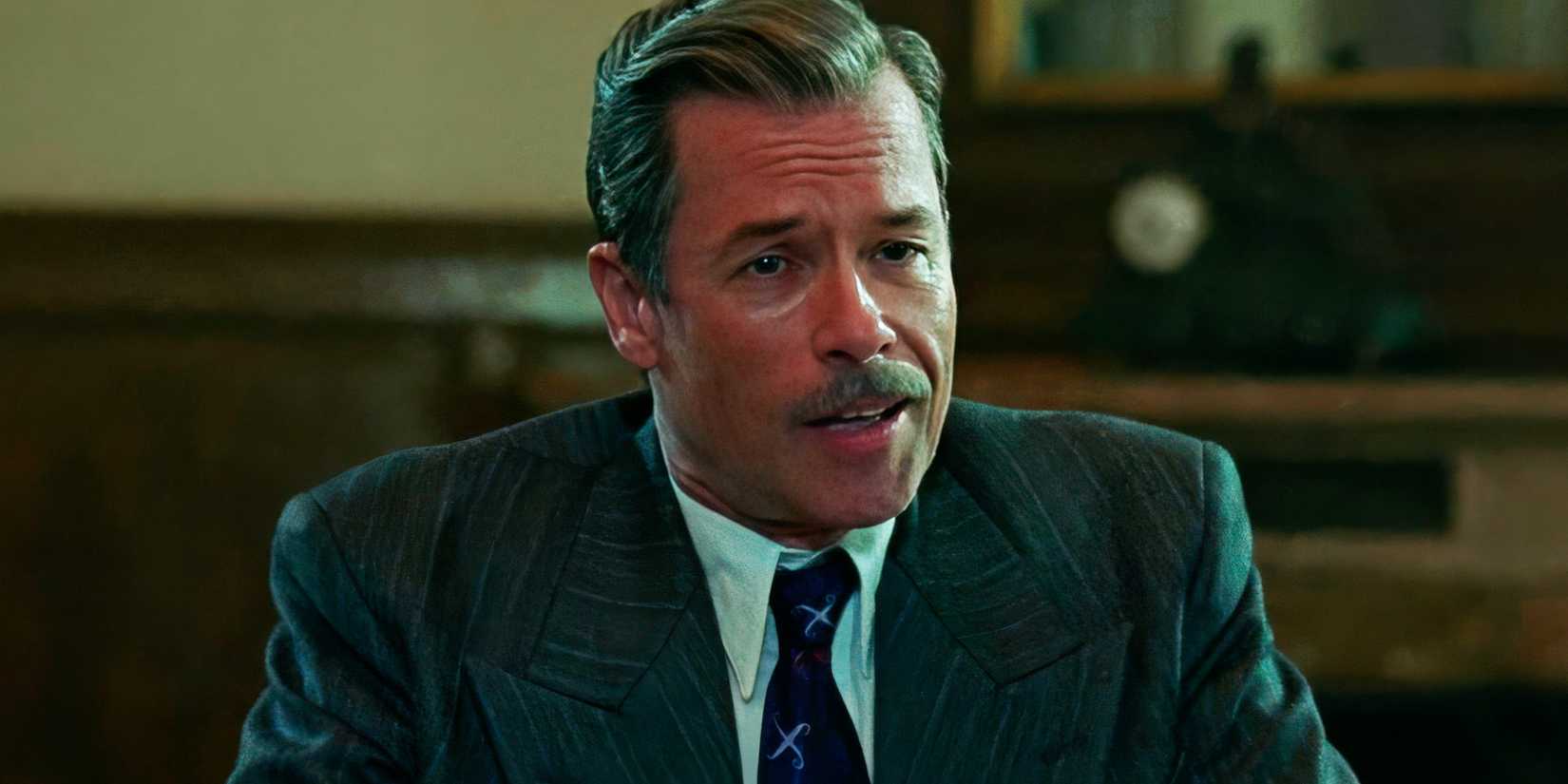 Guy Pearce as Harrison Lee Van Buren sitting down in The Brutalist.