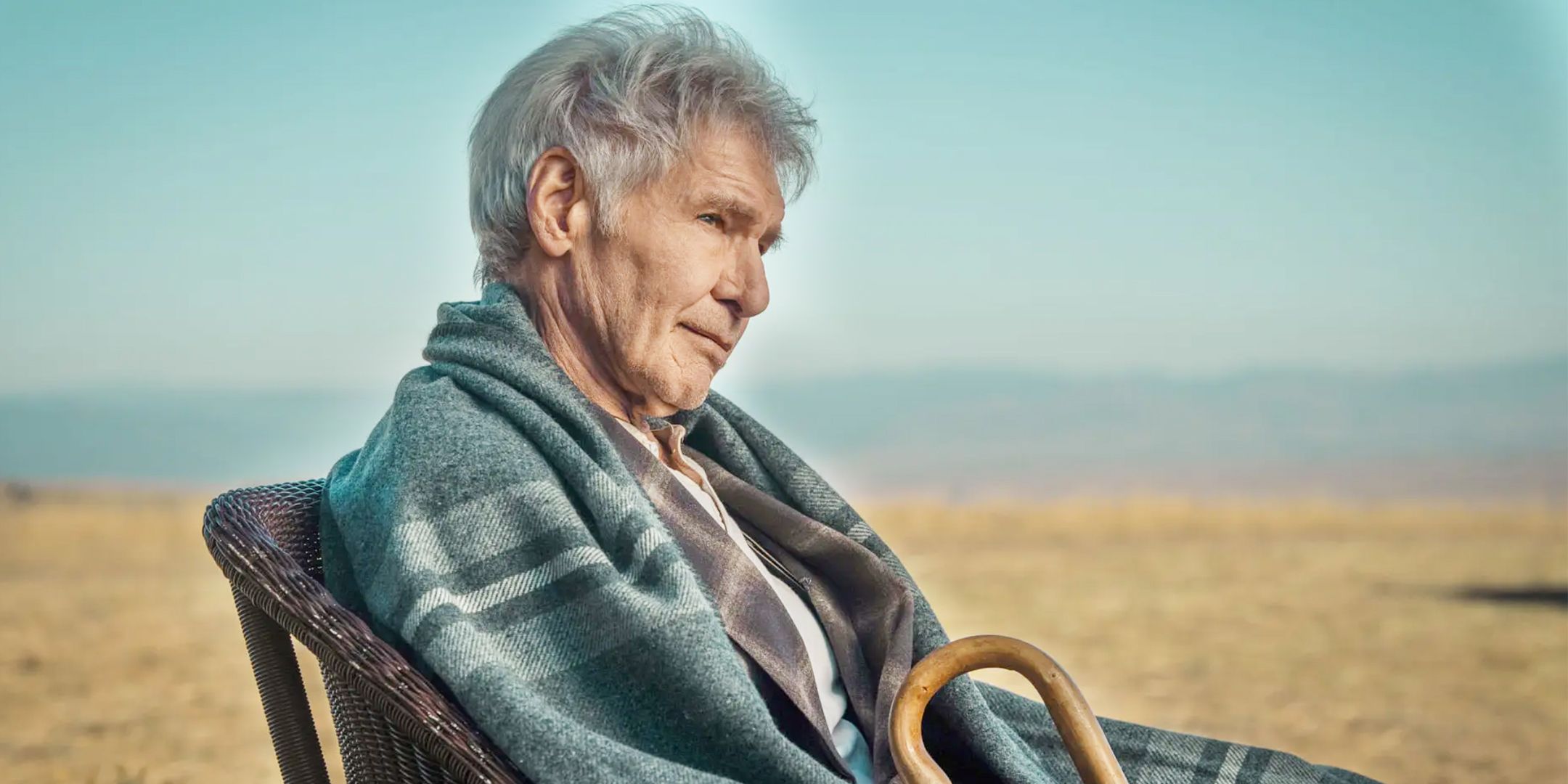Harrison Ford, as Jacob Dutton, sits in a chair with a blanket wrapped around him and a cane in his hand in the Yellowstone spinoff 1923.