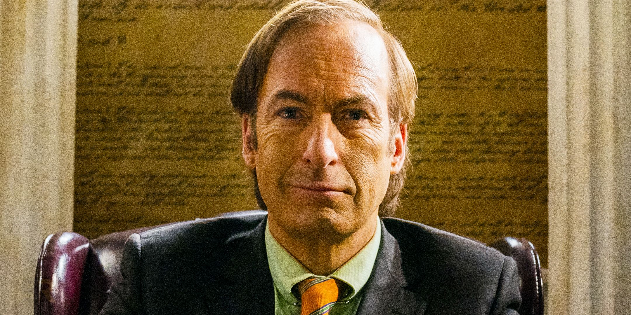 Jimmy McGill/Saul Goodman (Bob Odenkirk) smiling while sitting in his office in Better Call Saul season 6