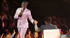 Jamal Roberts from American Idol wearing a shiny pearlescent suit fist bumping Luke Bryan while performing on stage.