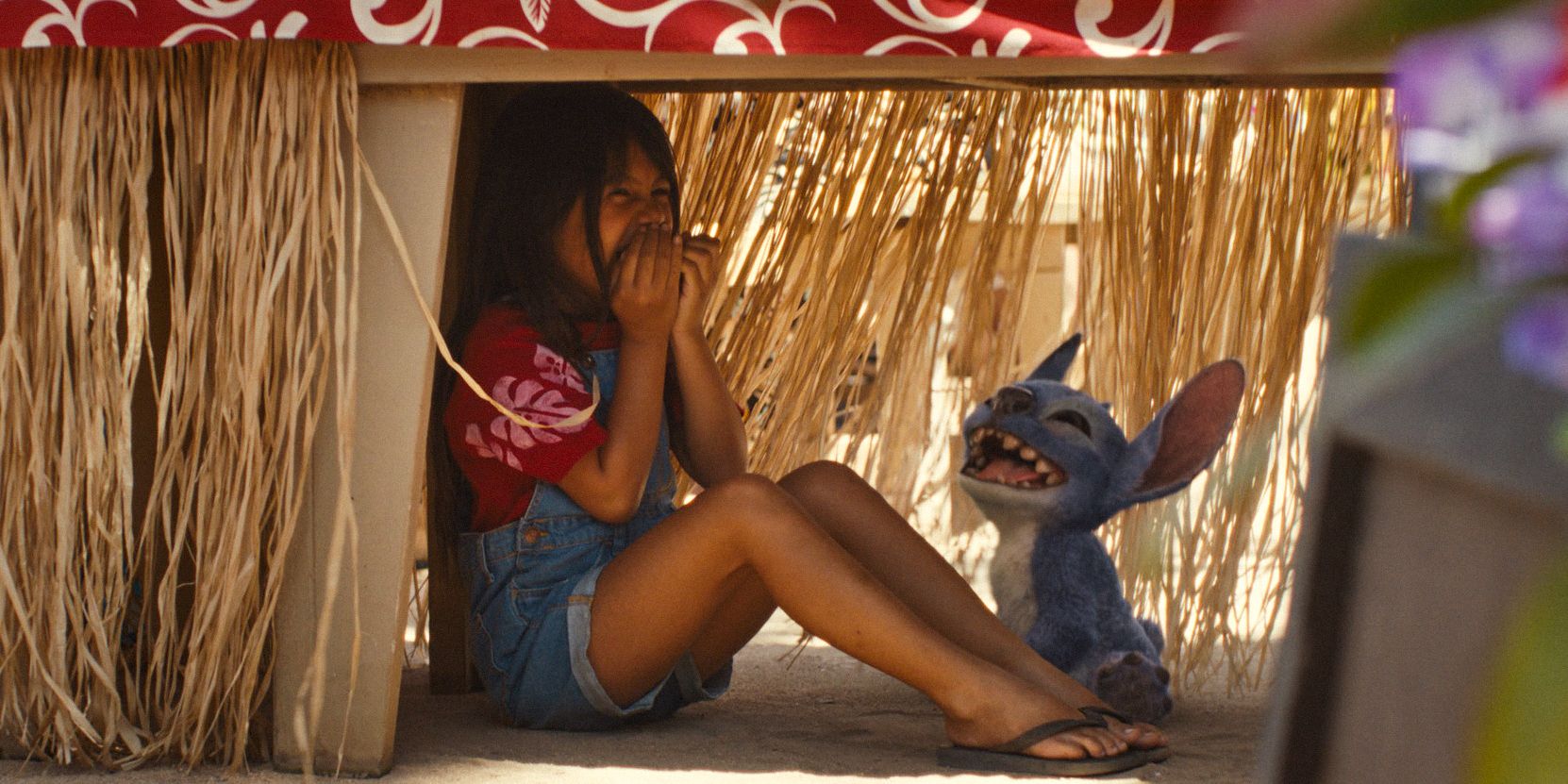 Lilo (Maia Kealoha) and Sтιтch laughing, hiding under a table in Lilo & Sтιтch (2025)