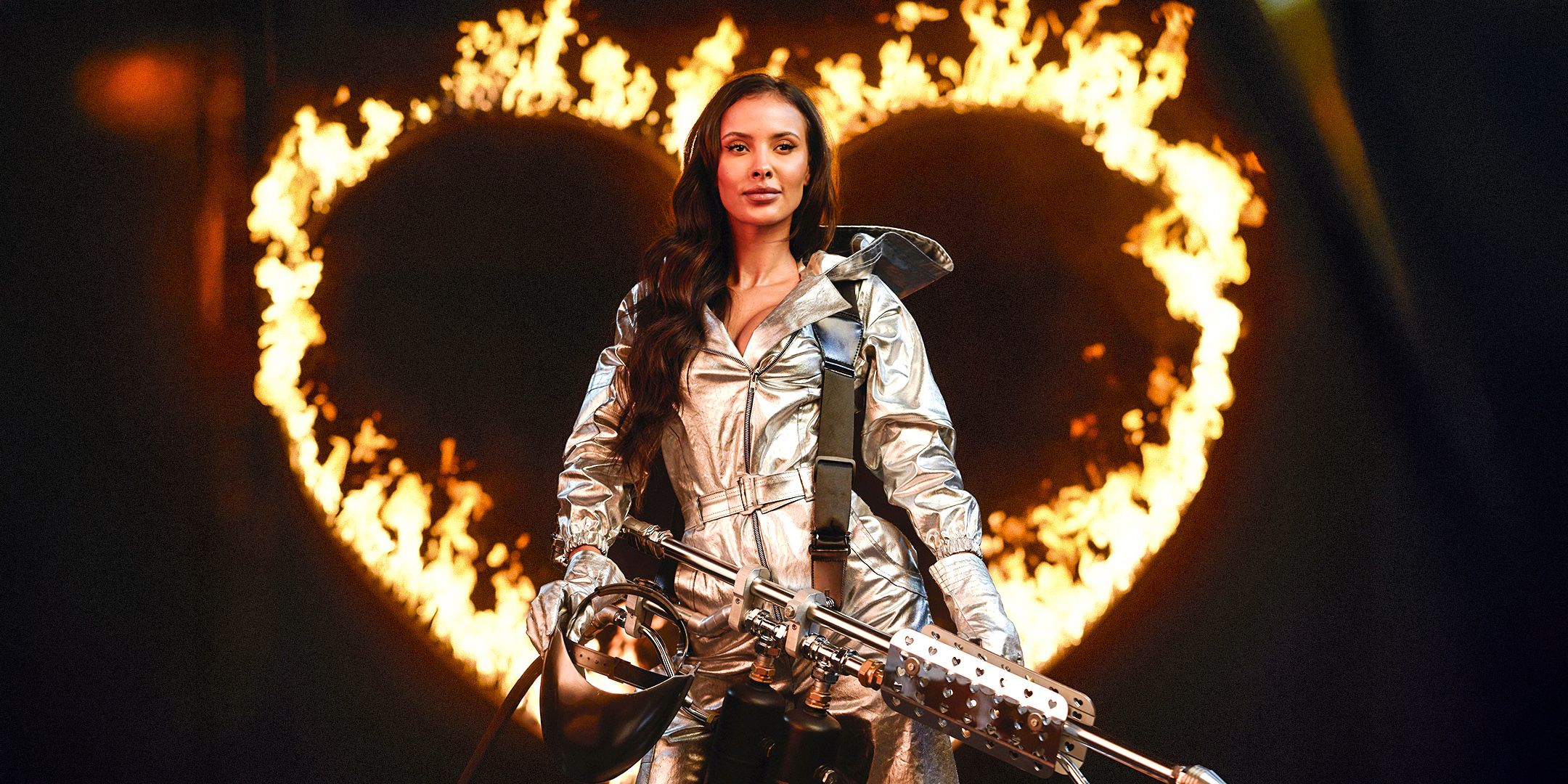 Love Island UK's Maya Jama holding a fire torch with a giant fire heart behind her
