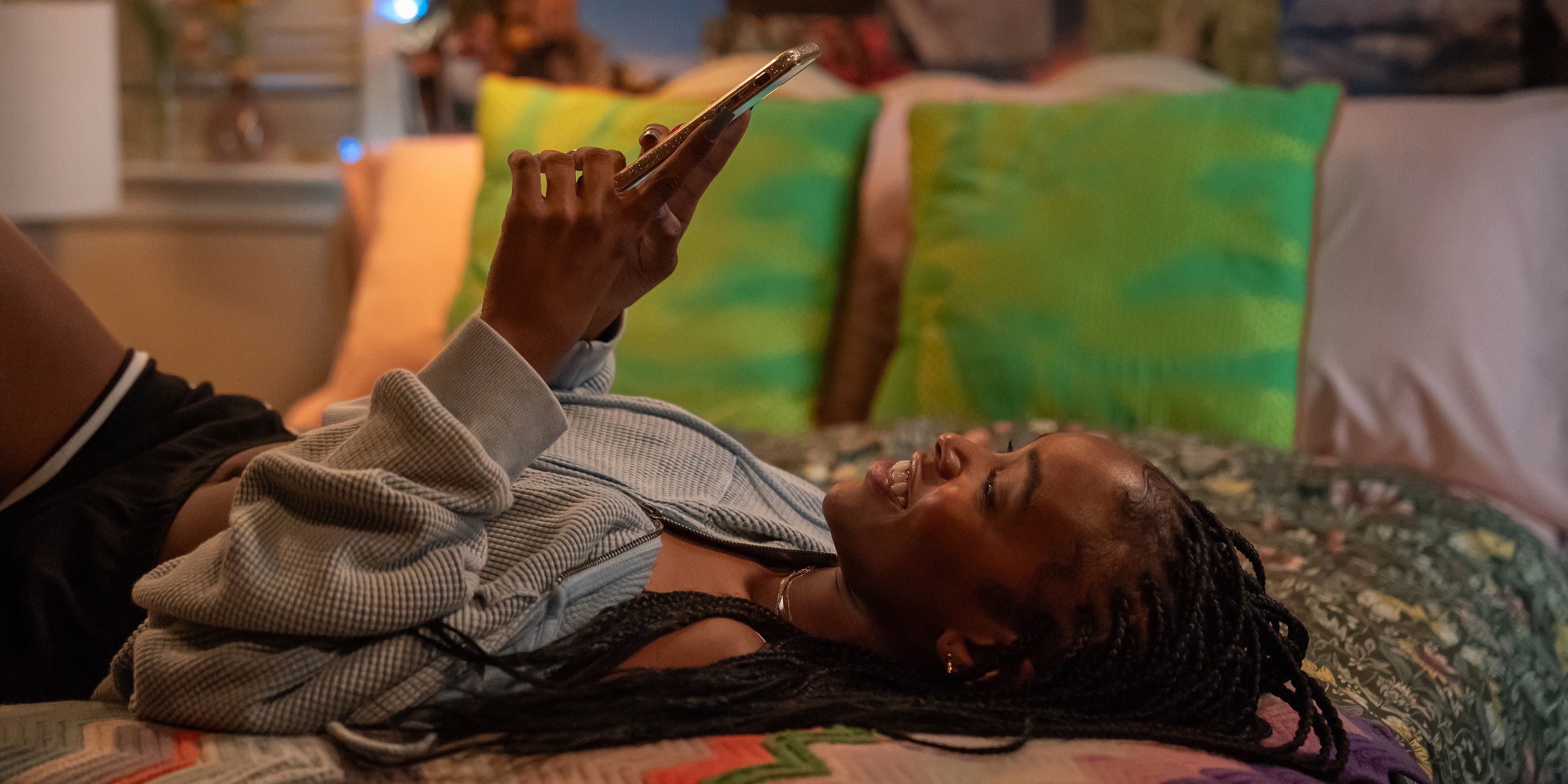 Lovie Simone as Keisha Clark lays on the bed and smiles at her phone in Netflix's Forever