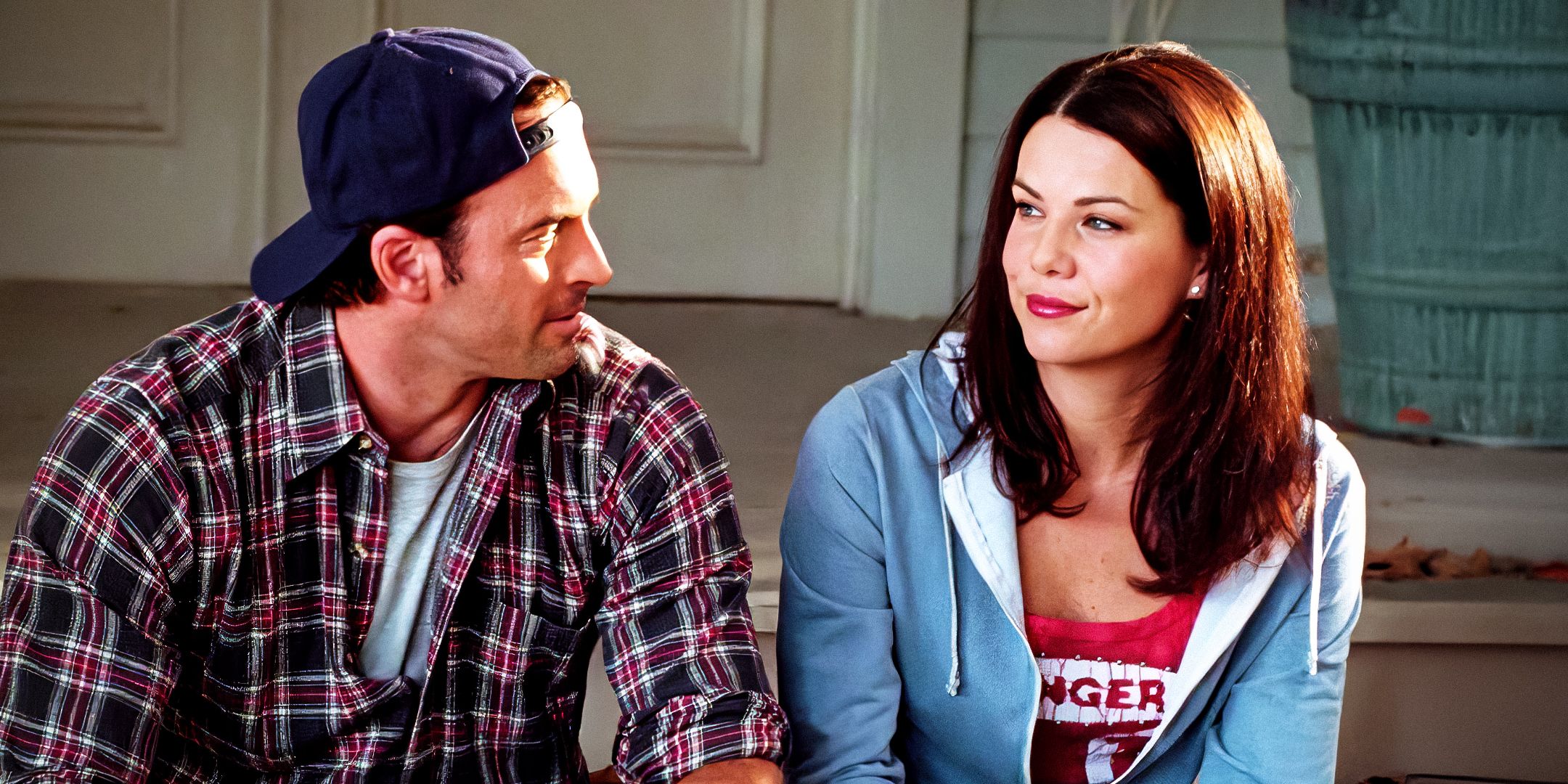 Luke And Lorelai looking at each other and smiling while sitting on the front steps of a house in Gilmore Girls.