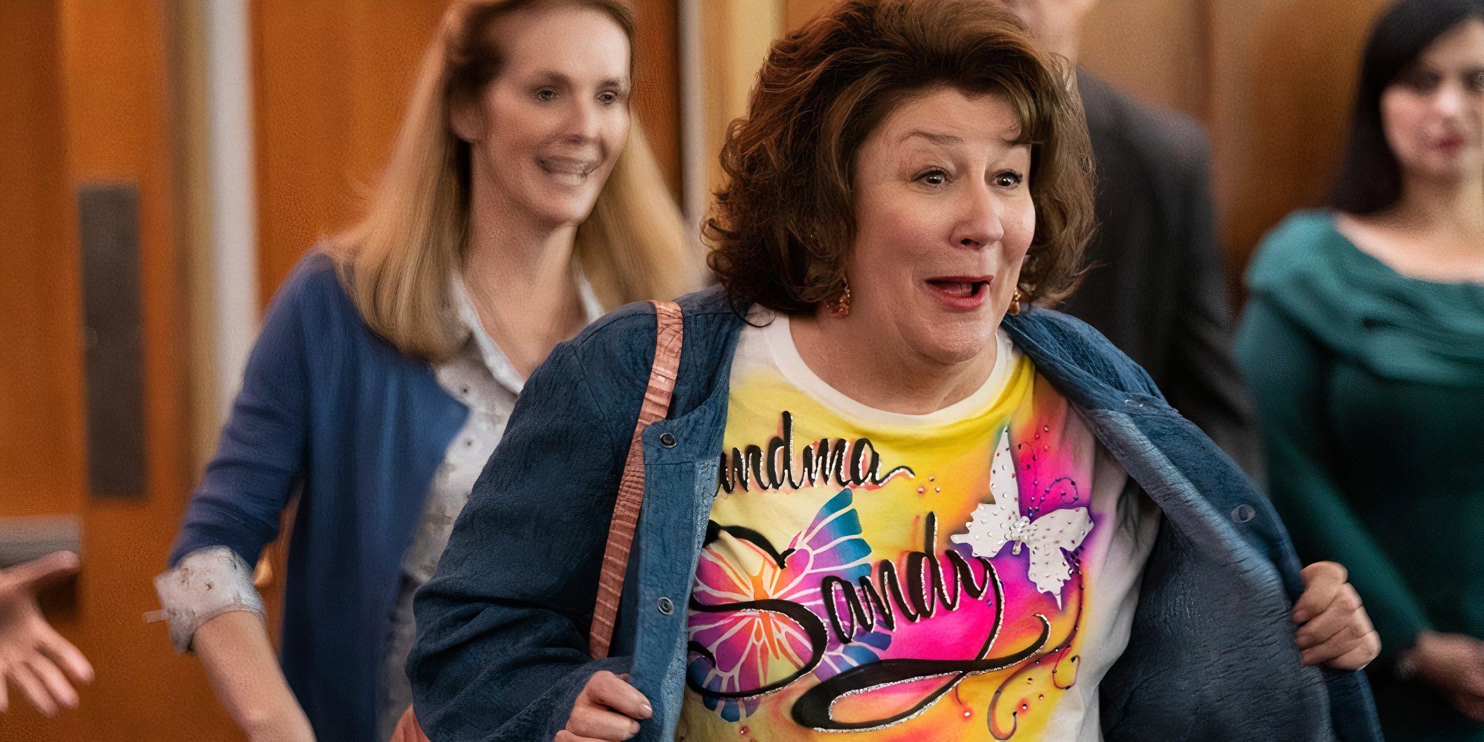 Margo Martindale excitedly flashes a colorful shirt that reads "Grandma Sandy." 