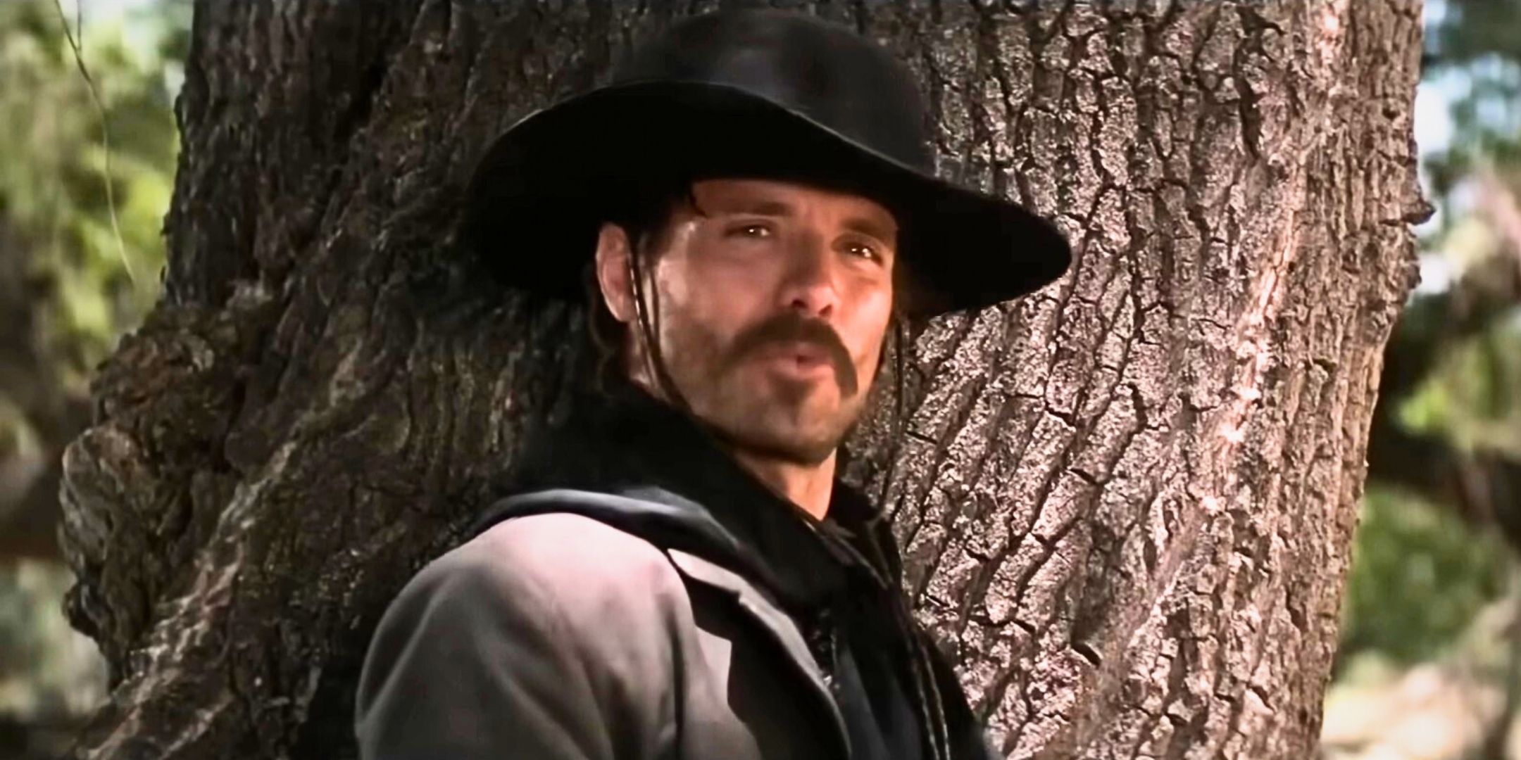Michael Biehn as Johnny Ringo standing by a tree in Tombstone