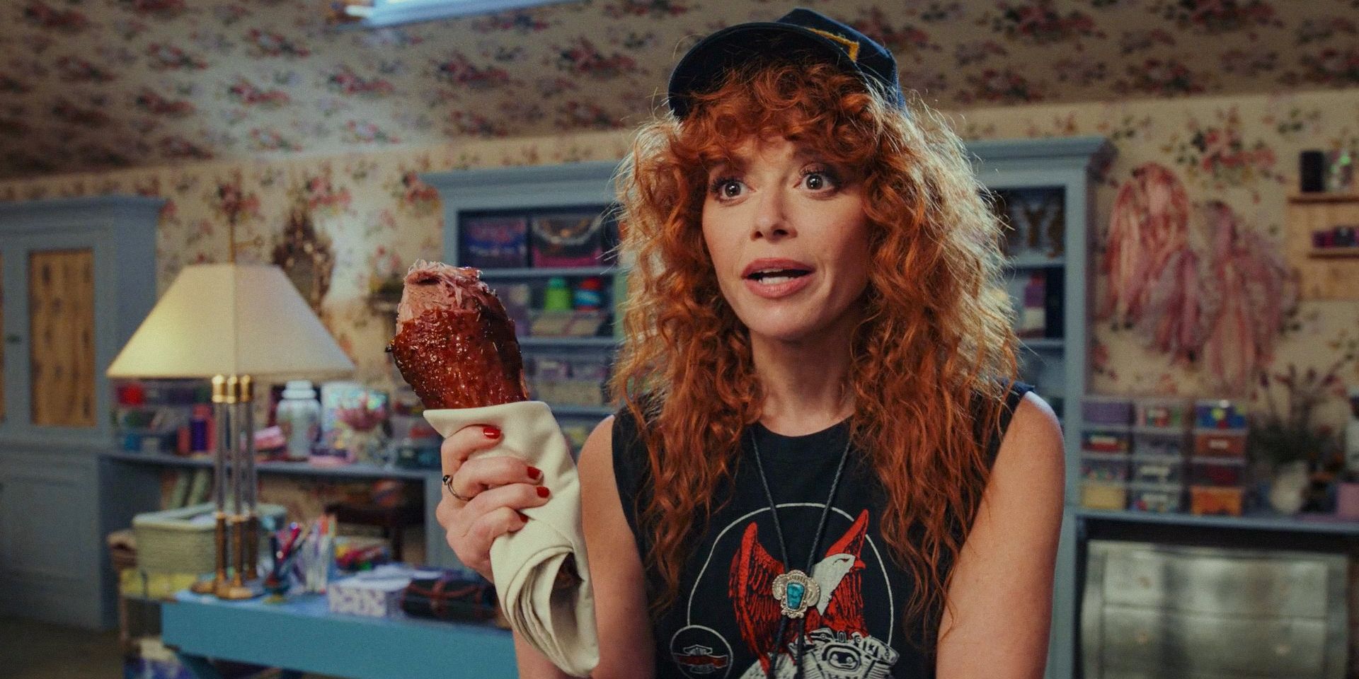 Charlie Cale (Natasha Lyonne) talking while holding a roasted leg in her hand in Poker Face Season 2 Ep 1