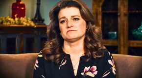 sister wives star Robyn Brown frowning in a black printed blouse in a living room