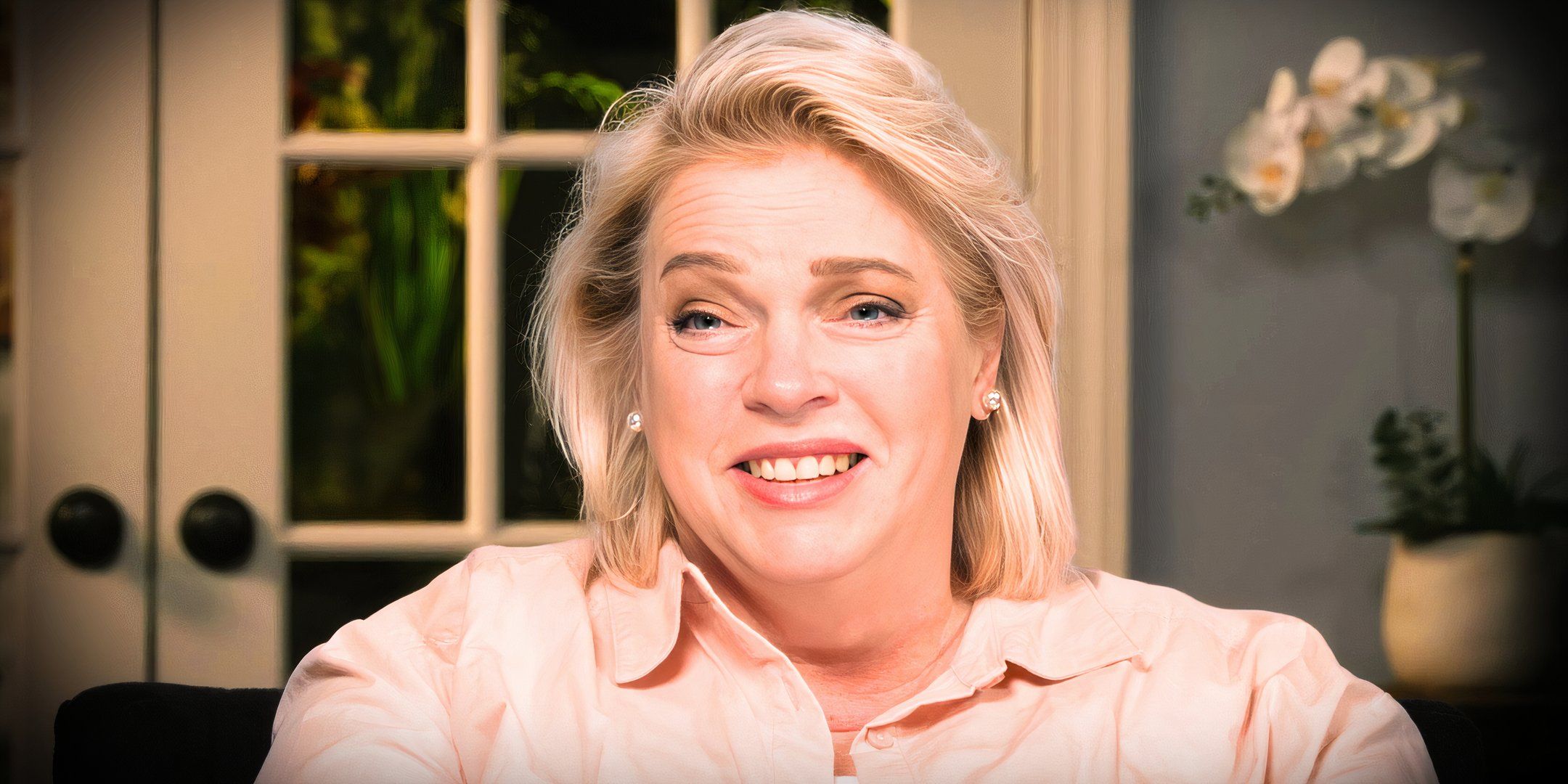 sister wives stars janelle brown in still of her in pale pink shirt smiling inside a home