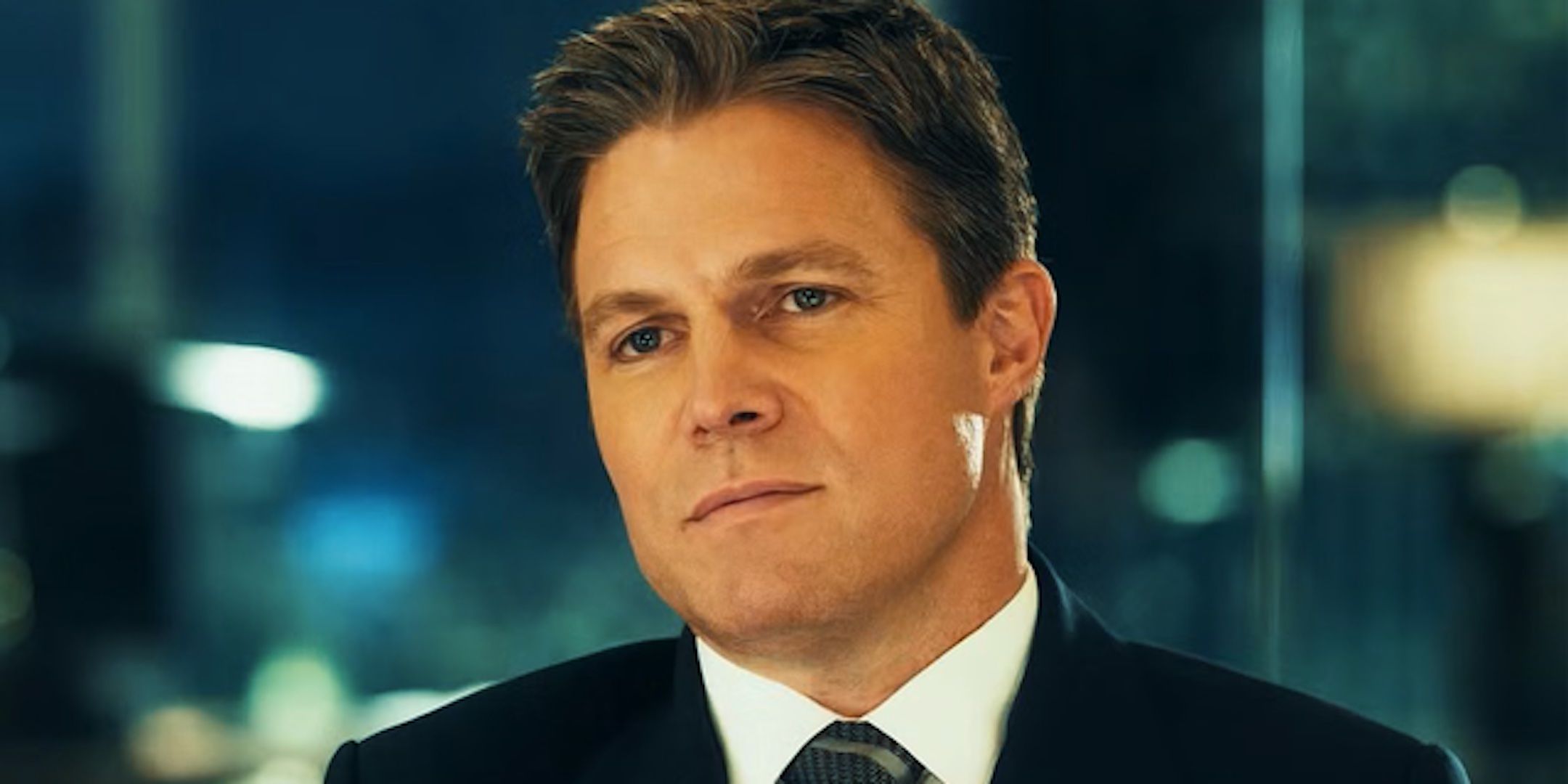 Stephen Amell's Ted Black frowns sitting a table from Suits LA