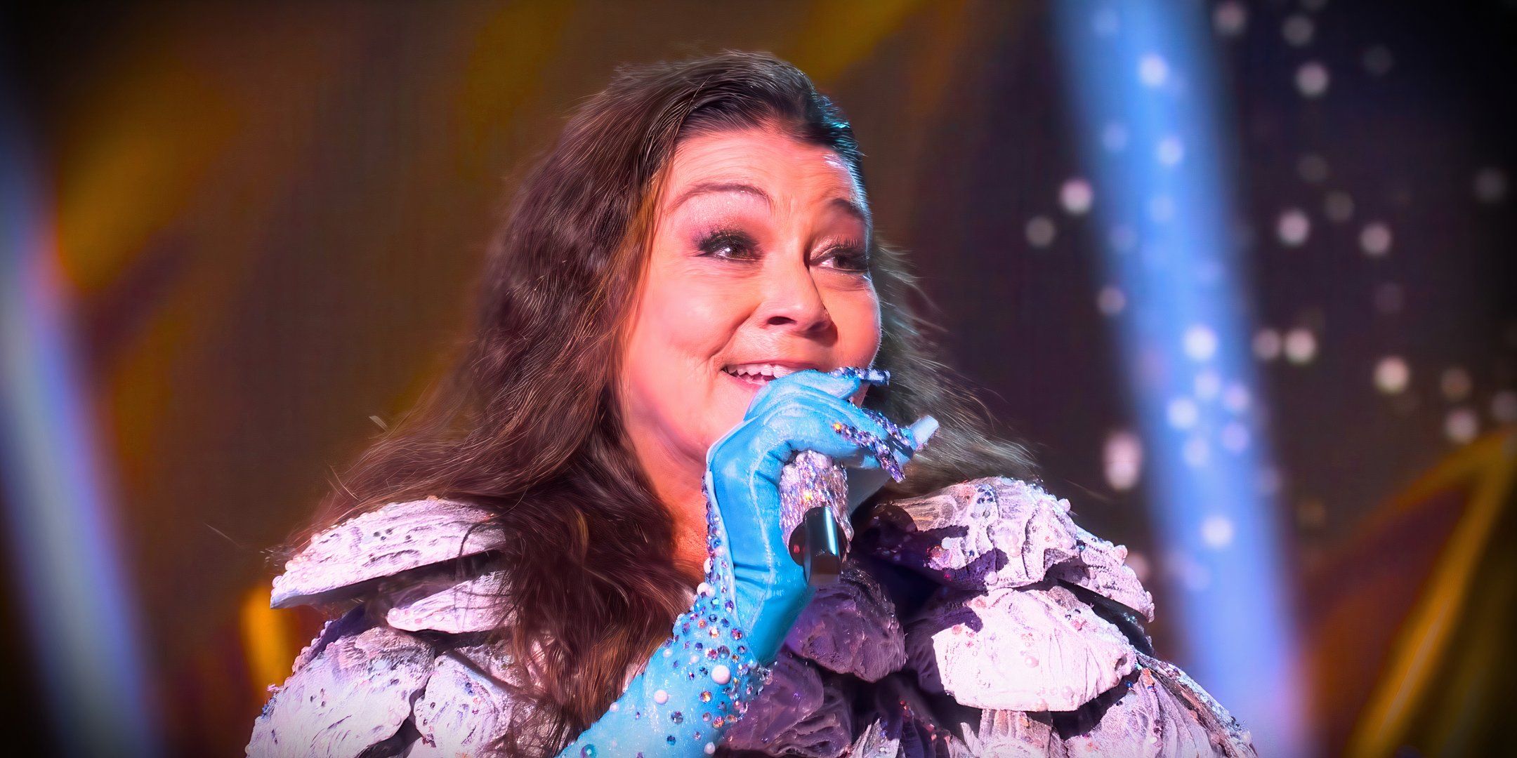 still of gretchen wilson from the masked singer performing with blue gloves on and smiling