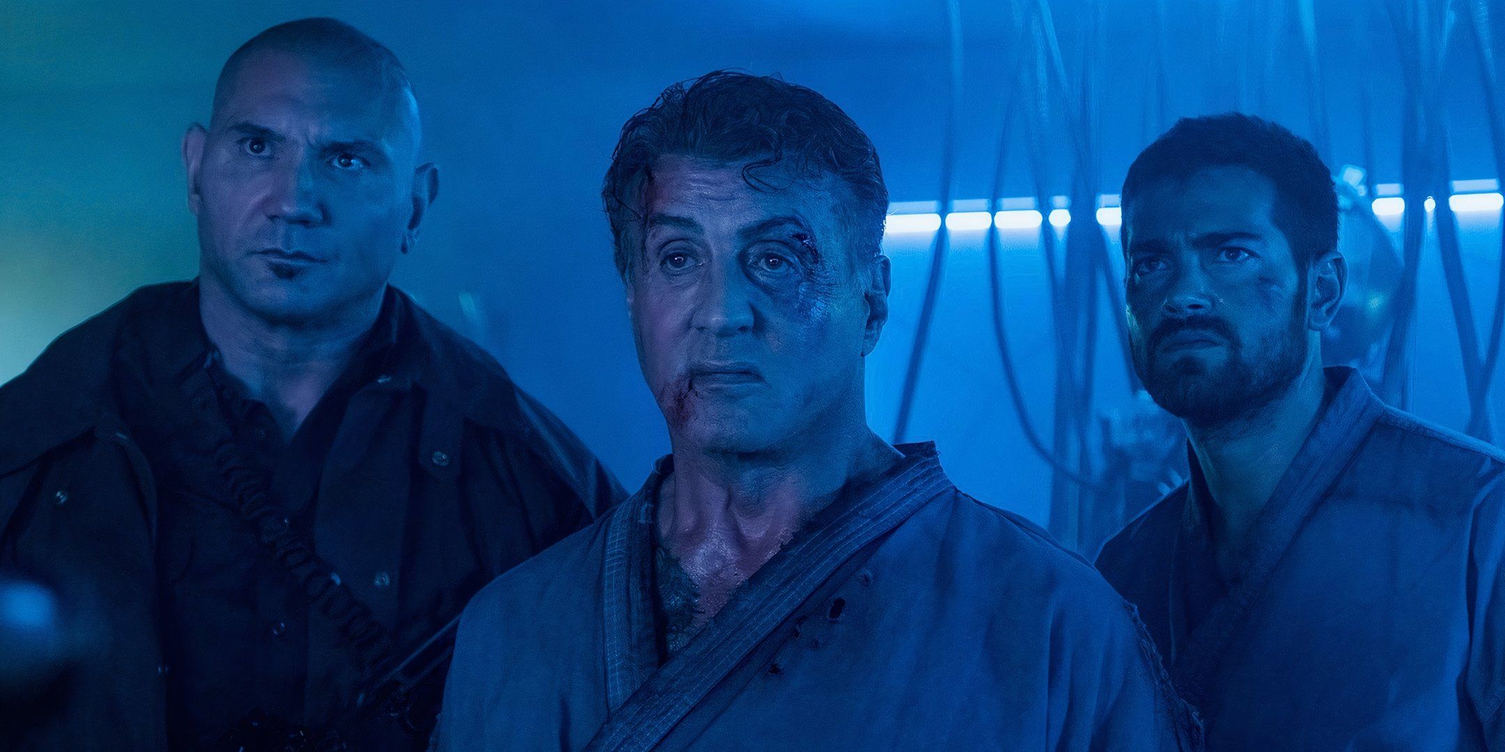 Dave Bautista, Sylvester Stallone, and Jesse Metcalfe stand in a line next to one another.