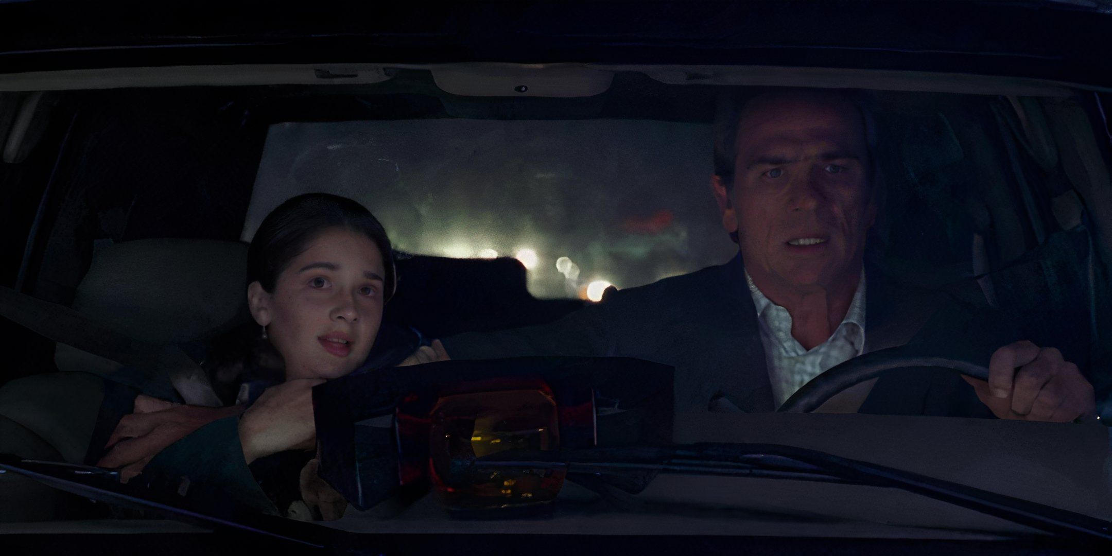 Tommy Lee Jones worriedly holds onto Gaby Hoffmann in the front seat of a car.