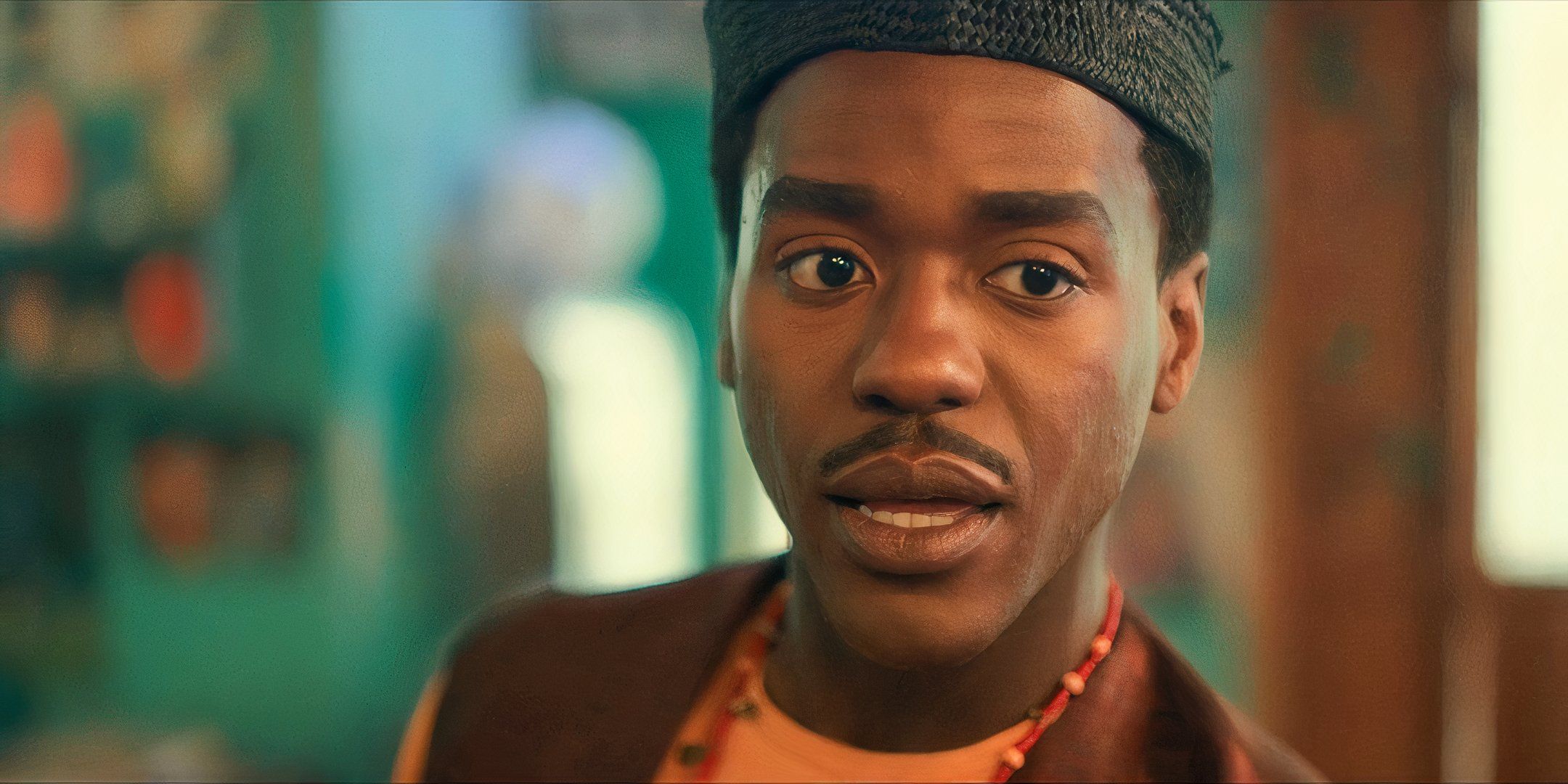 Ncuti Gatwa as the Fifteenth Doctor, wearing a dark orange vest, orange shirt, beaded necklace, and knit cap