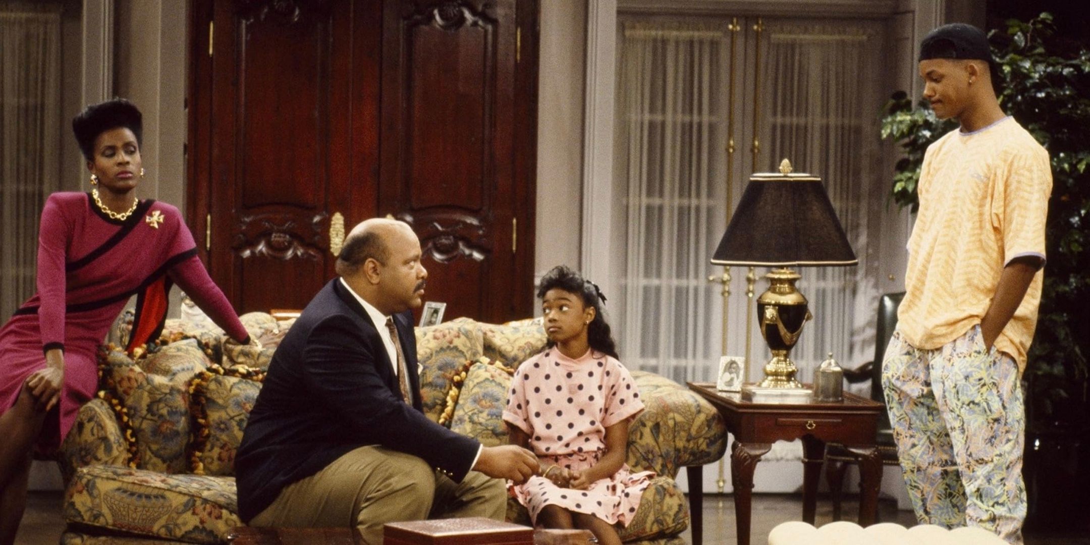 Janet Hubert, James Avery, and Tatyana Ali sit on a couch while Will Smith stands to the side of them. 
