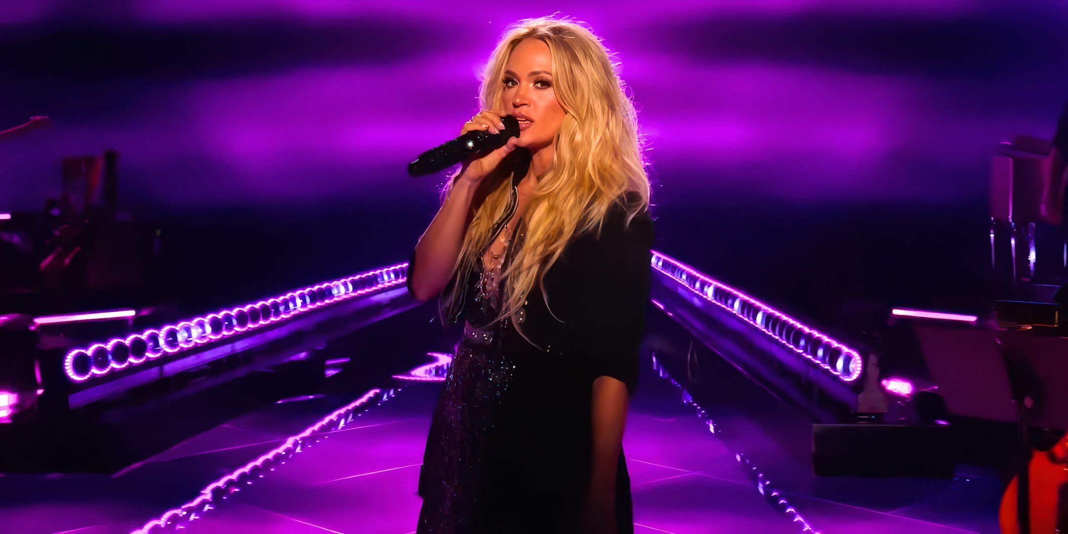 american idol judge carrie underwood singing onstage with long hair and purple lighting