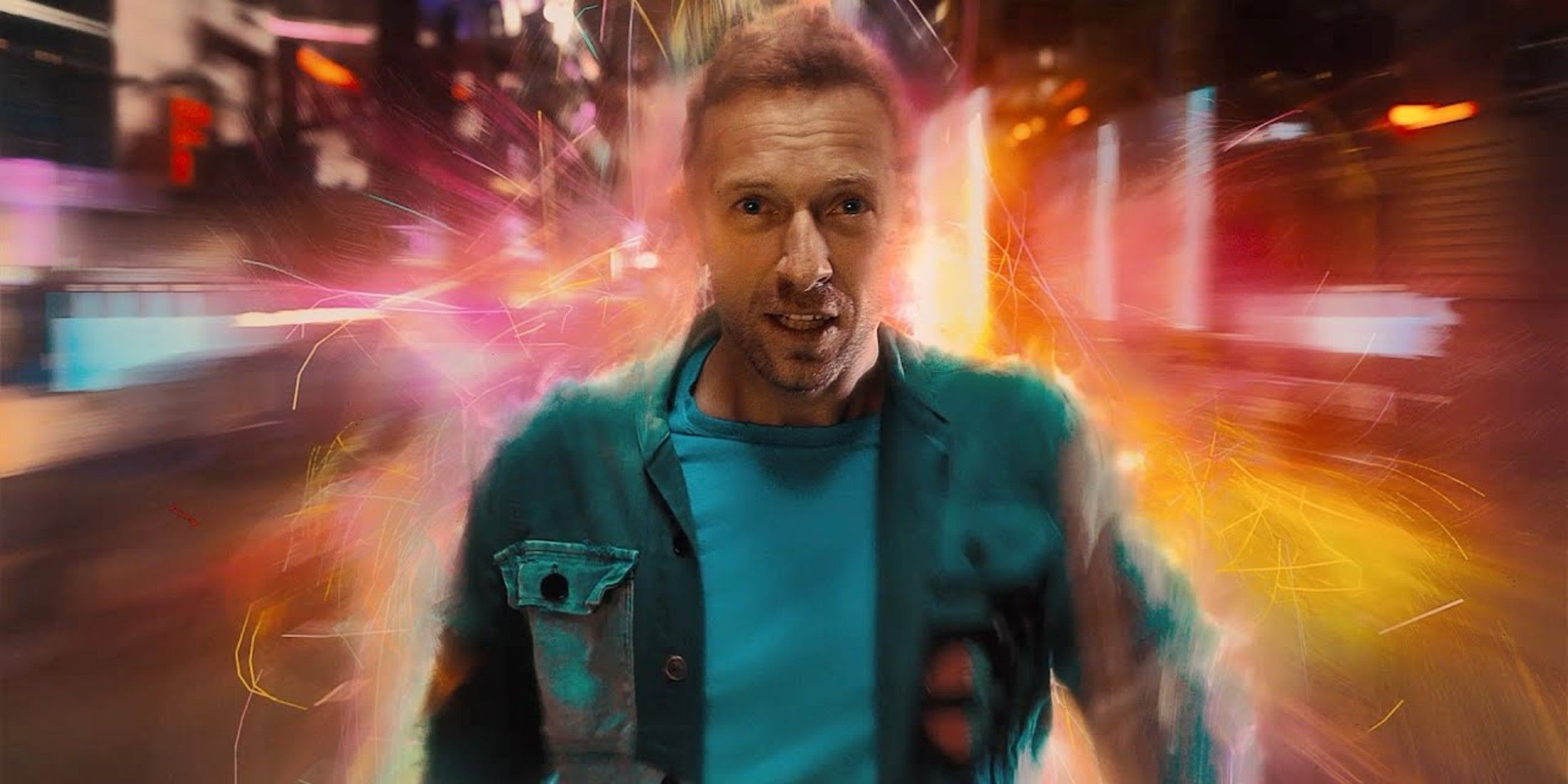 O fundo é embaçado, mas é colorido. Chris Martin, do Coldplay, é o único número. Ele é mostrado do peito, vestindo uma camisa azul e uma jaqueta azul. 