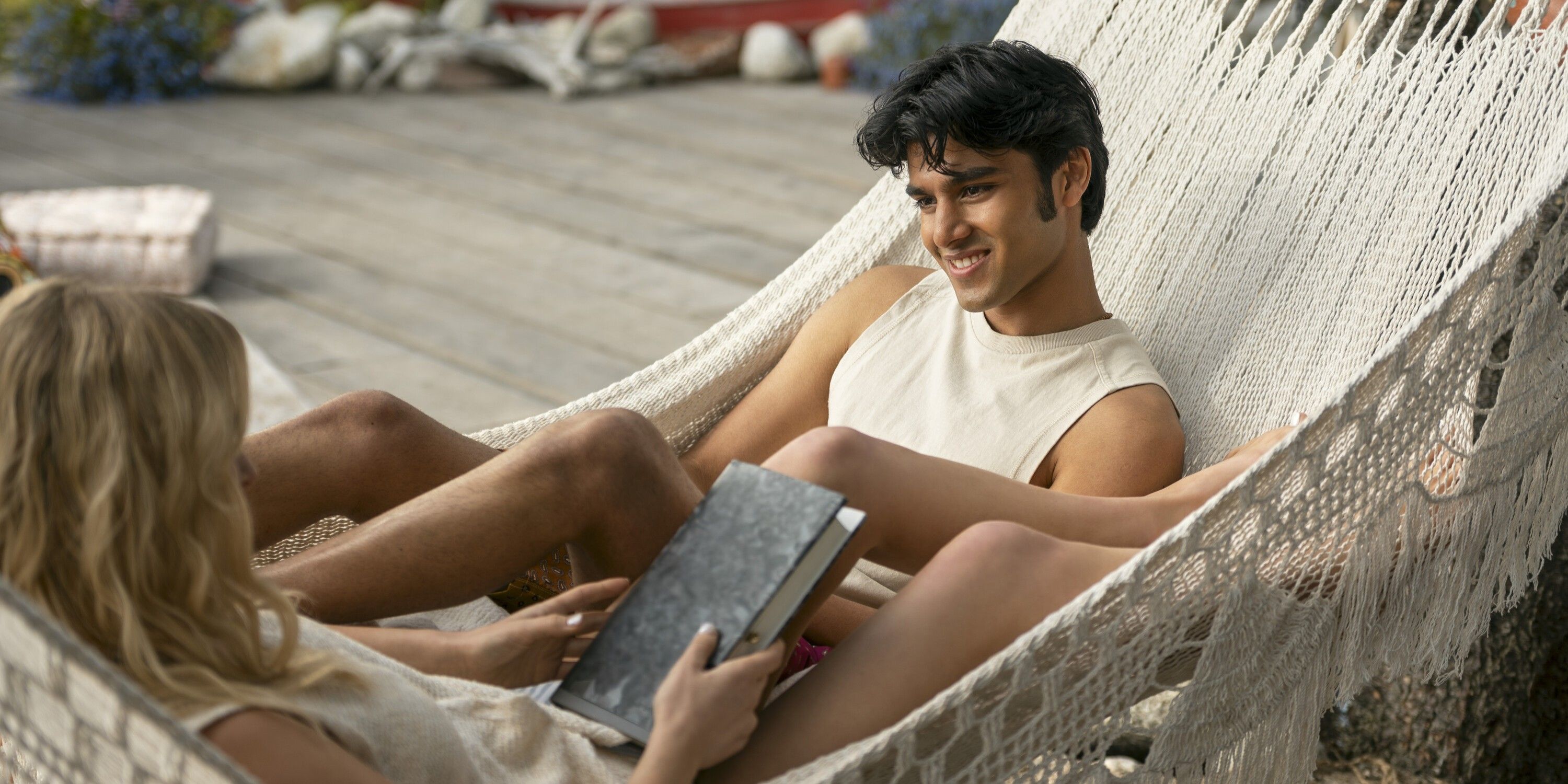 Gat sits in a hammock smiling with Cadence in Prime Video's We Were Liars