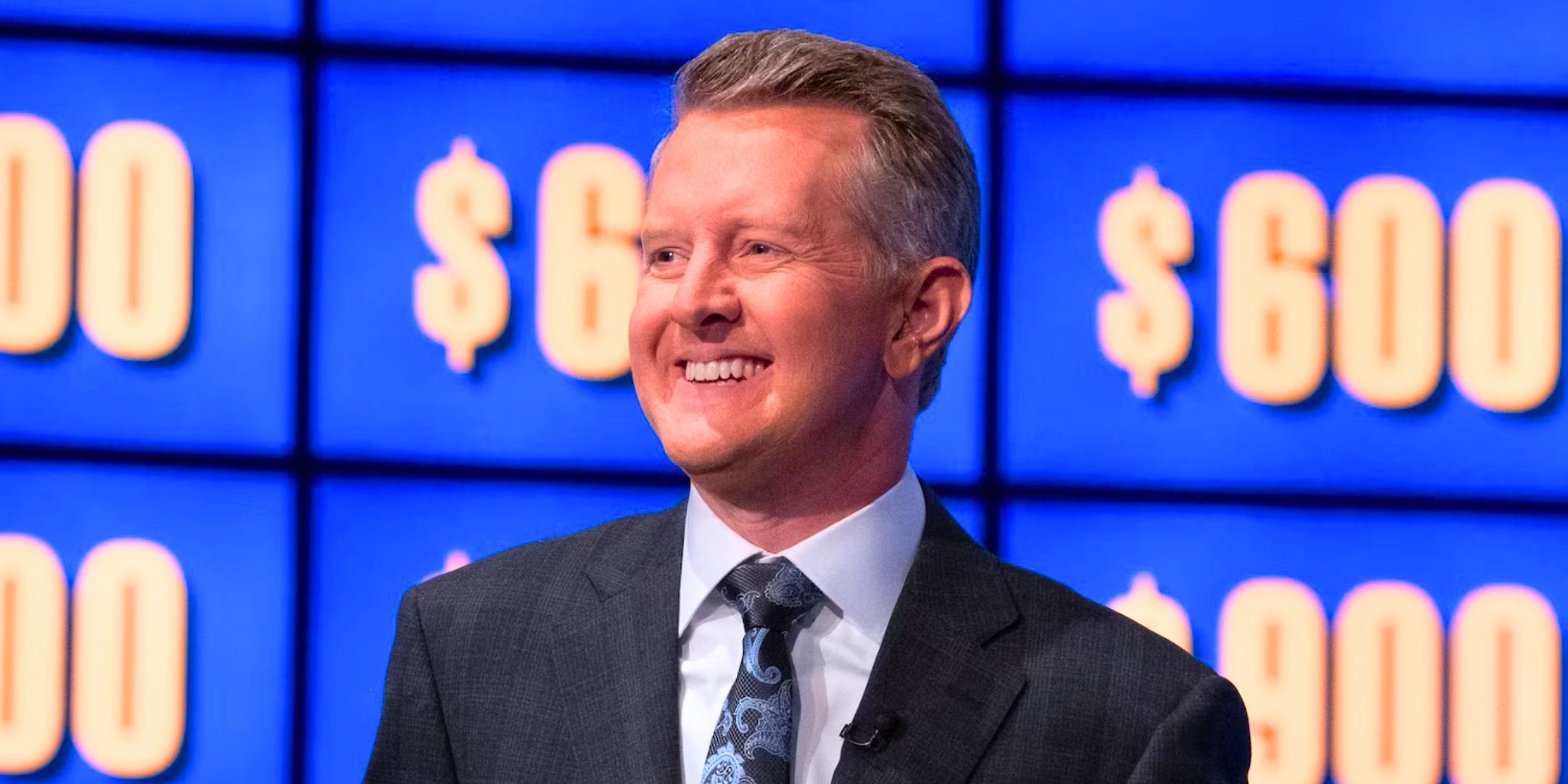 Ken Jennings smiles in front of the Jeopardy category board