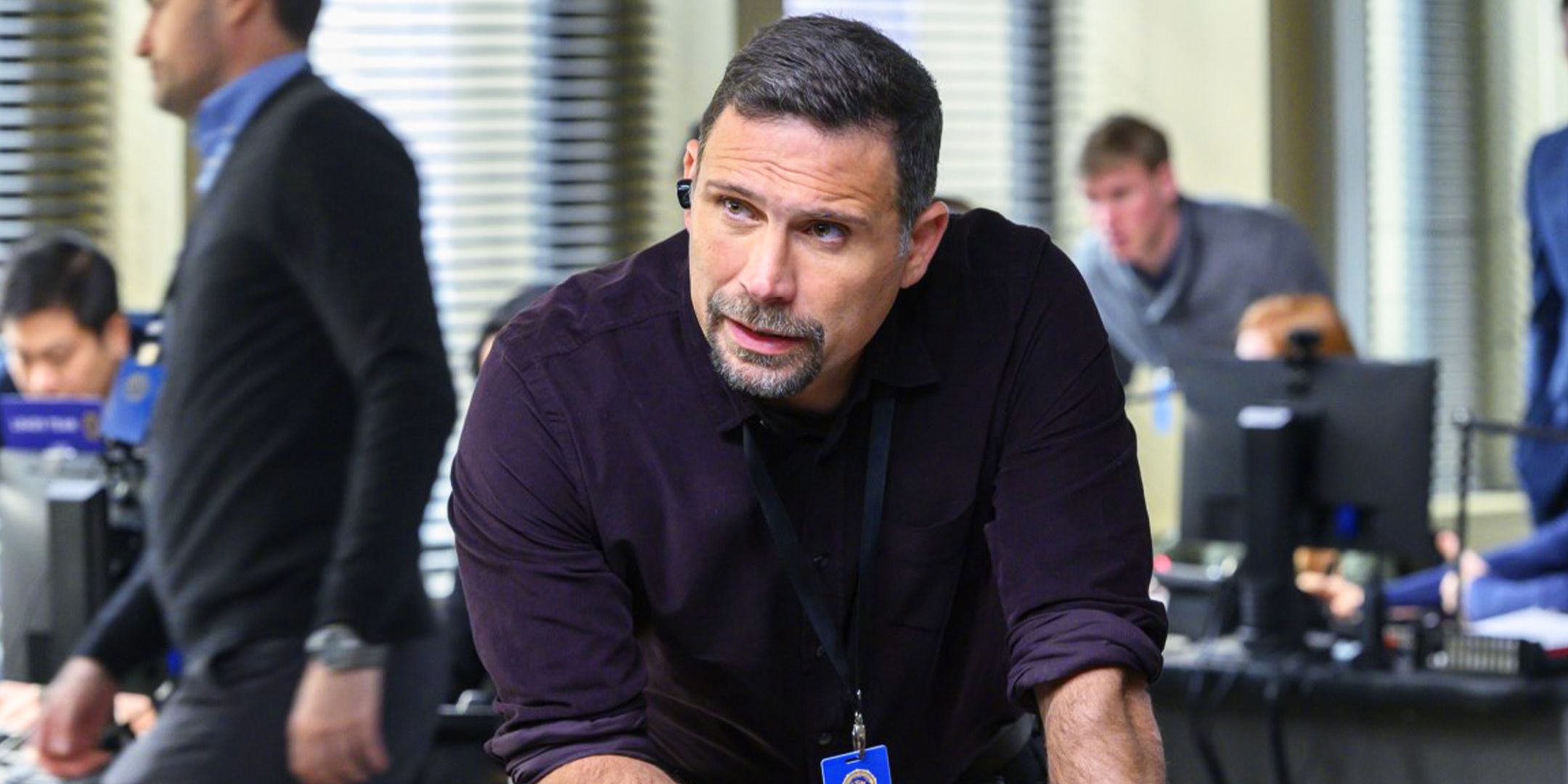 Jubal stands in the FBI headquarters with his earpiece in giving and receiving info about a case