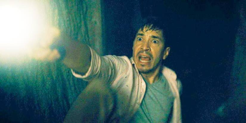 Justin Long looking scared and shining a flashlight in Barbarian