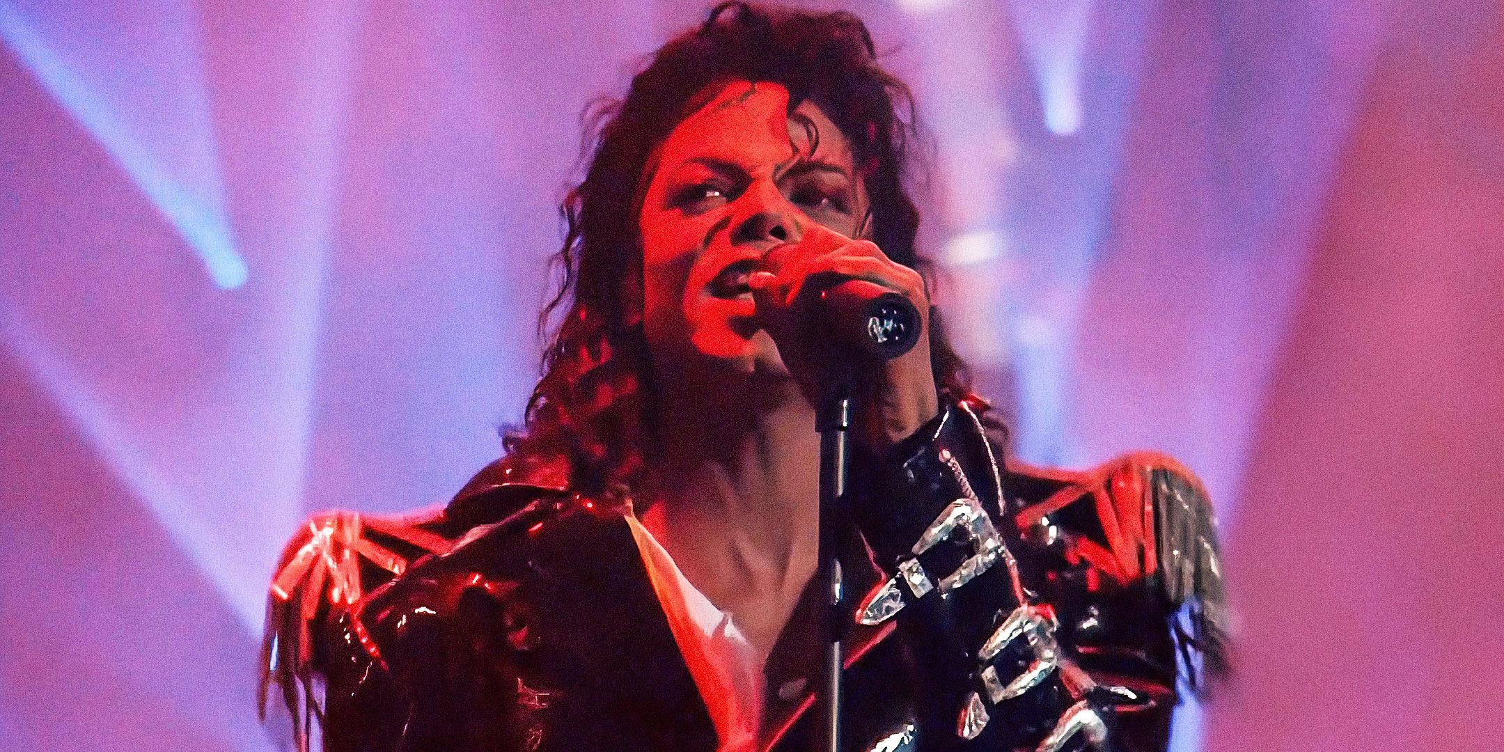 Michael Jackson wears a black leather jacket and sings into a microphone in his 1988 music video for "Come Together."