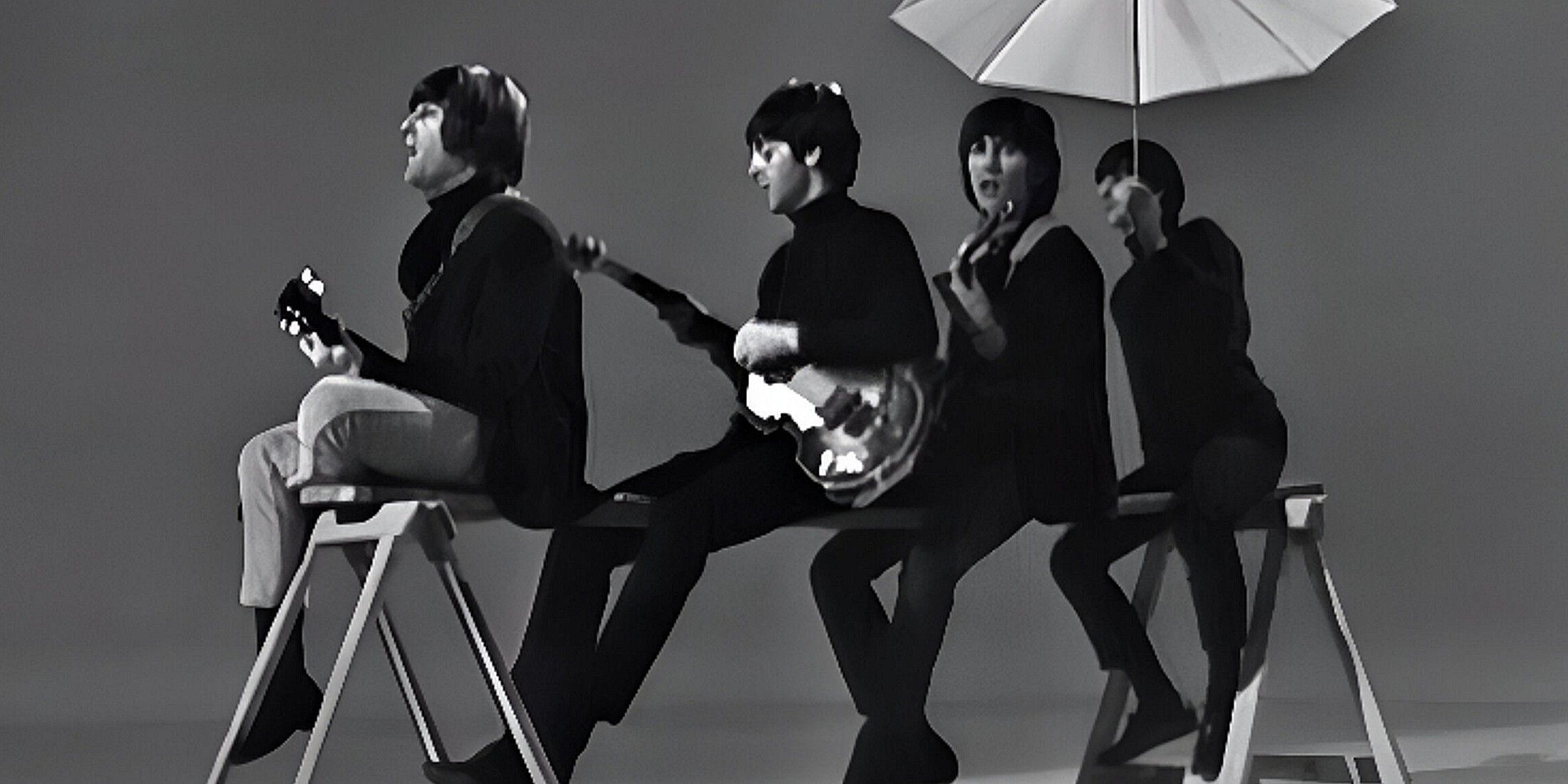 The pH๏τo is in black and white. The four Beatles all sit on a wooden plank, wearing jeans and long sleeve shirts. Three of them hold guitars, while the one in the back holds an umbrella.