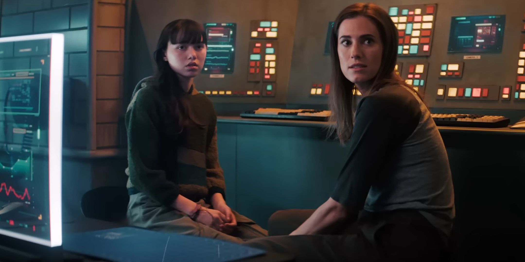 Violet McGraw's Cady and Alison Williams' Gemma looking worried while sitting next to a control panel in M3GAN 2.0