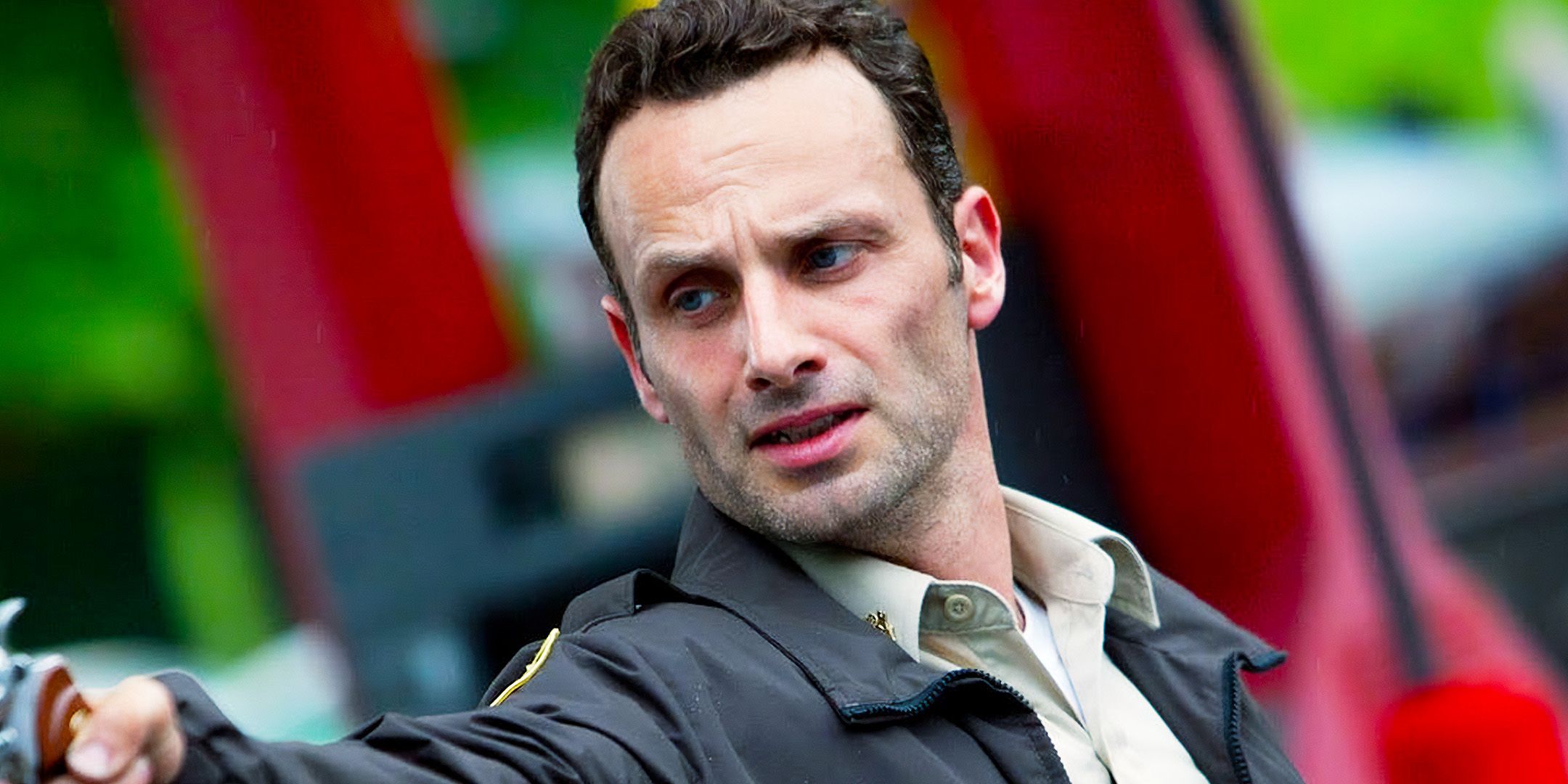 Rick Grimes aiming a gun at someone offscreen looking emotional in The Walking Dead