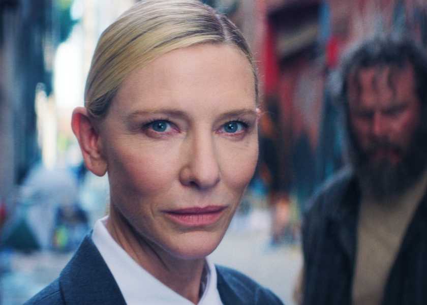 Cate Blanchett as the Recruiter smirking towards the camera while a bearded man stands behind her in Squid Game Season 3 Episode 6